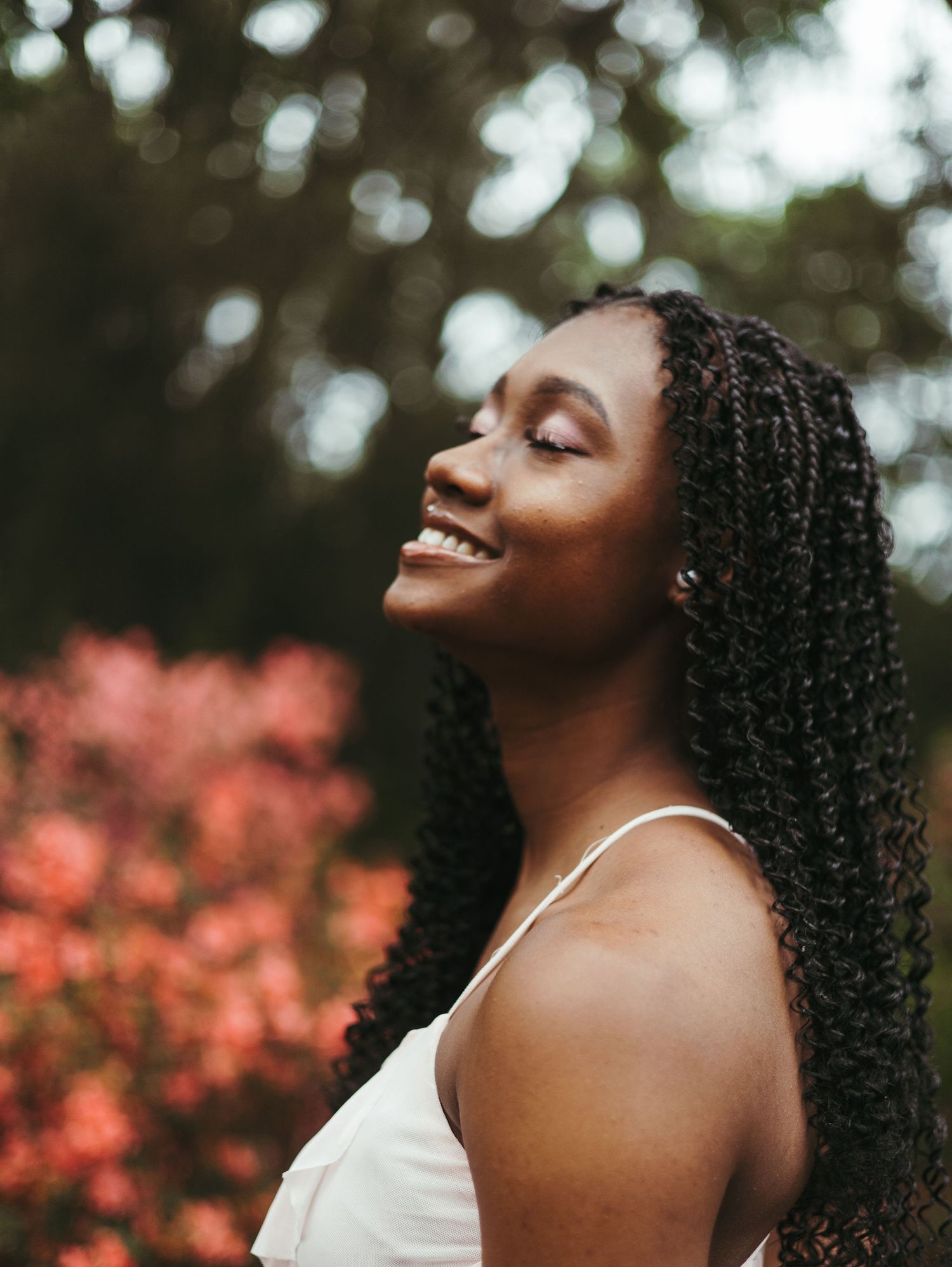 A joyful moment captured in nature with curly hair and white top against a blurred background of pink flowers and greenery.