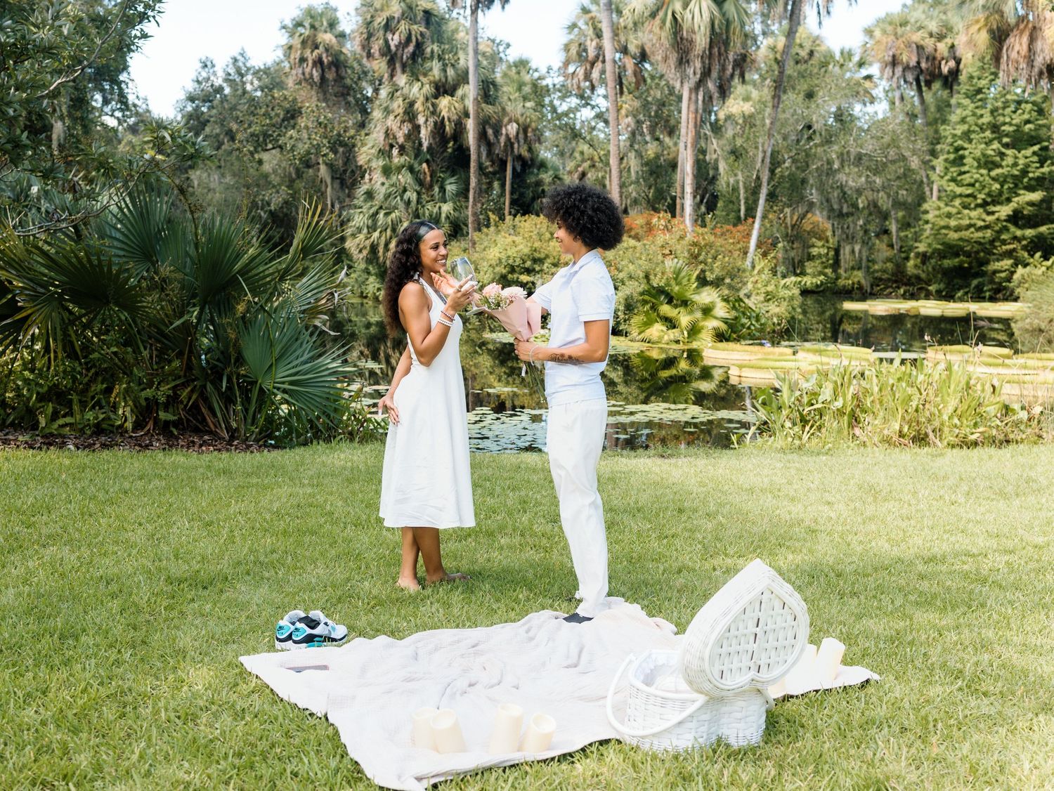 One white picnic blanket carefully spread out on a lush green grass lawn near tropical palm trees.