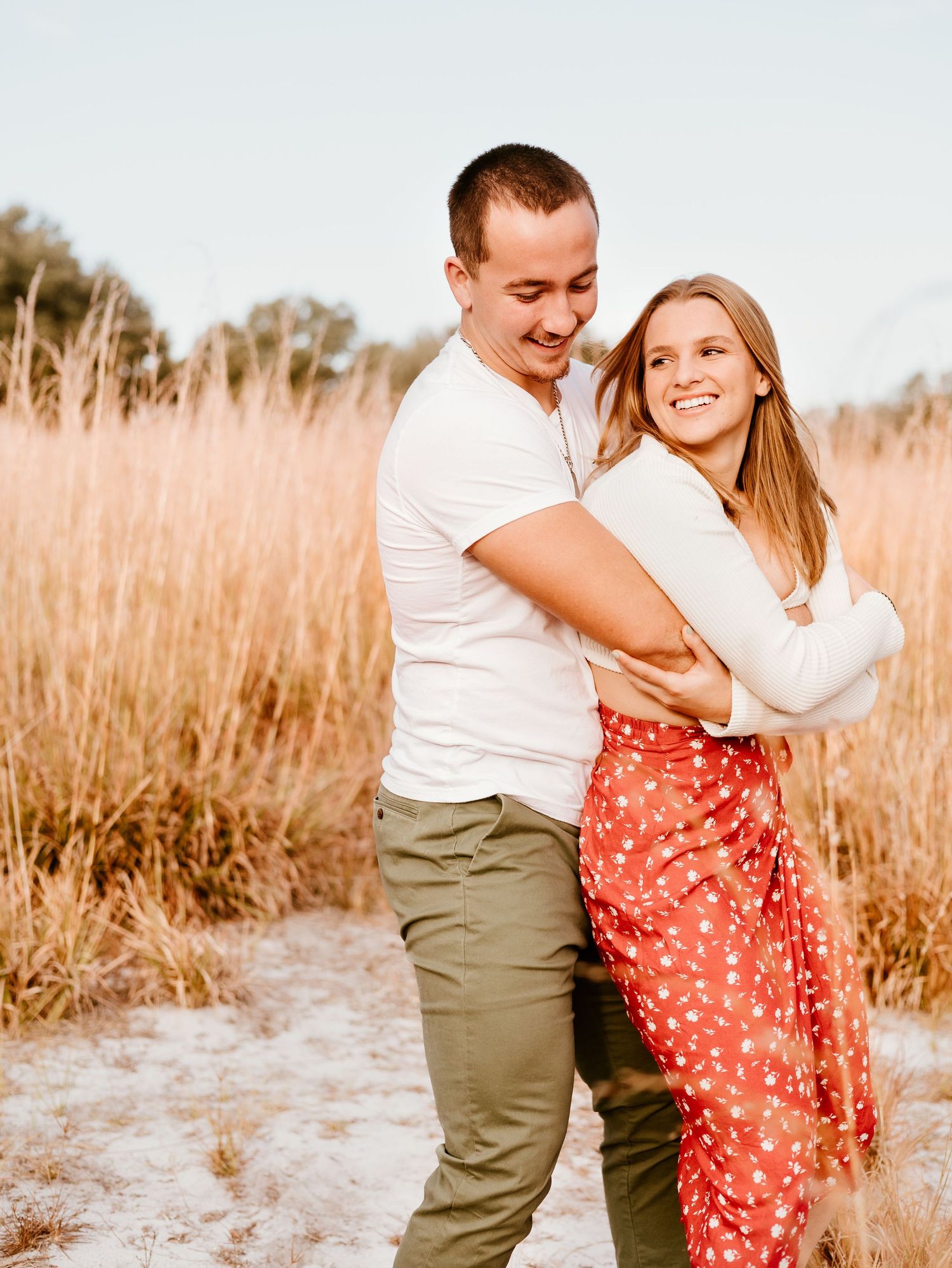 A romantic couple embraces and laughs together in a golden field at sunset creating a joyful outdoor portrait.
