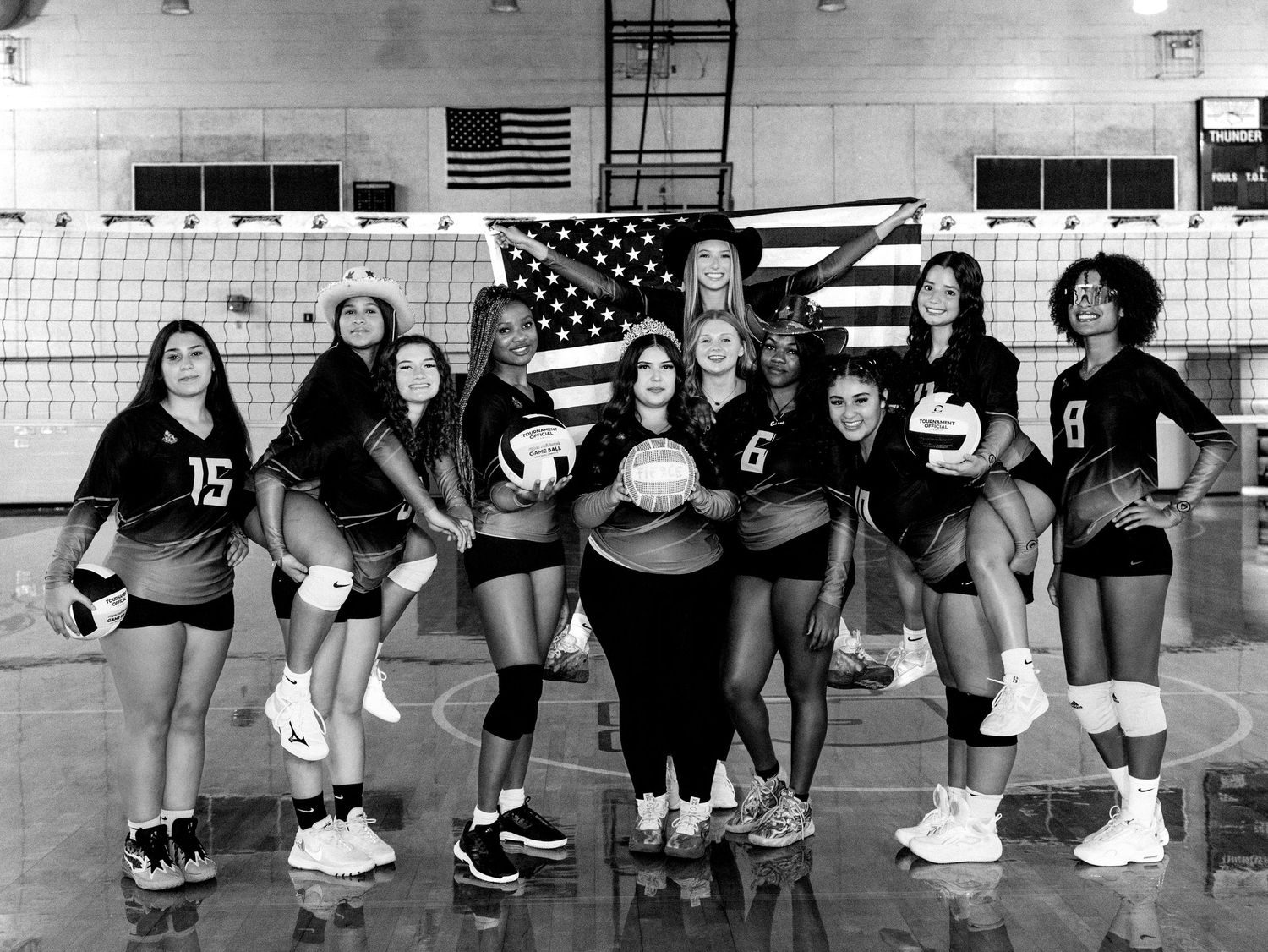 A group of volleyball players link arms in a synchronized line formation across a gymnasium court.