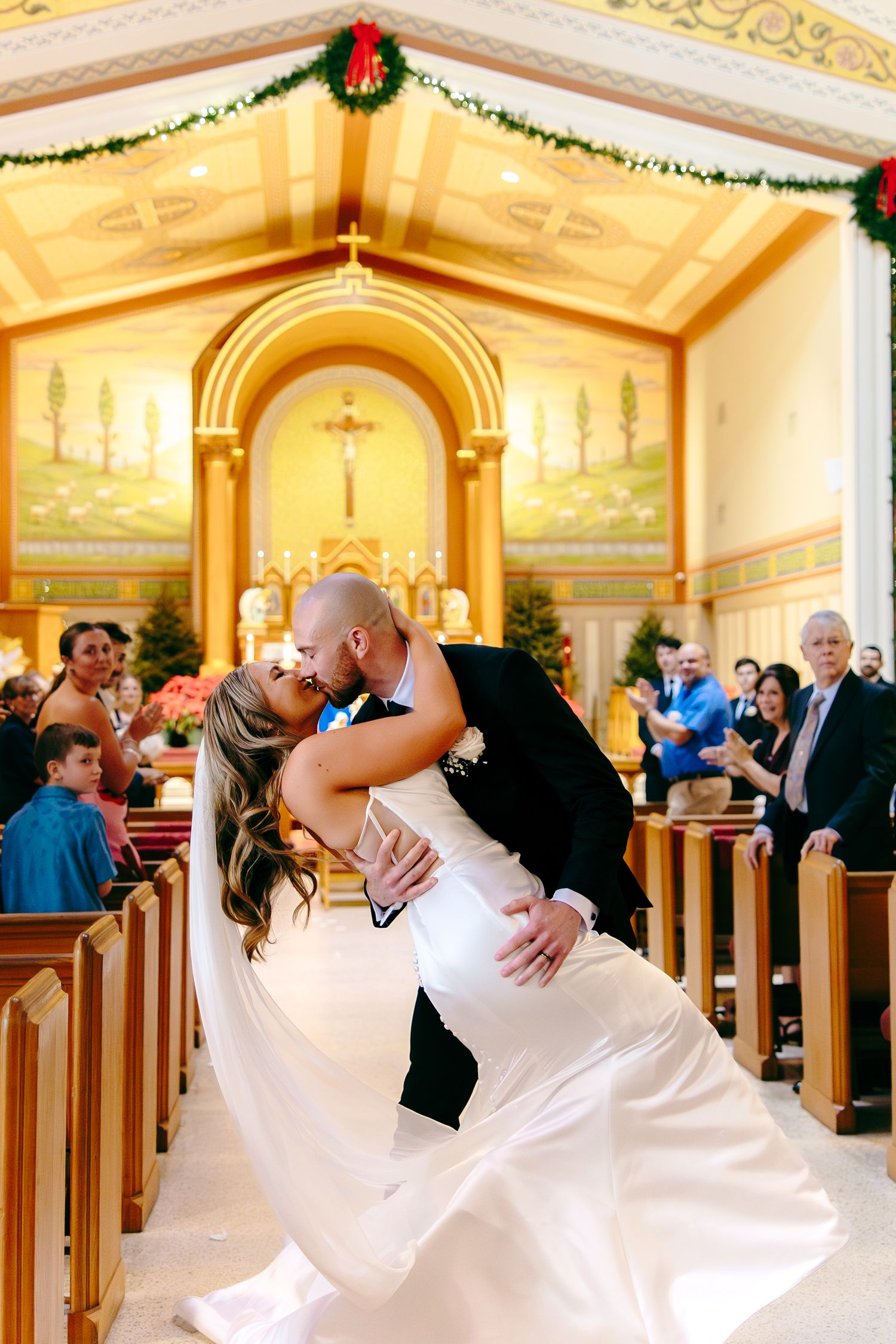 Groom dips bride for a kiss in a decorated church aisle during their wedding ceremony.