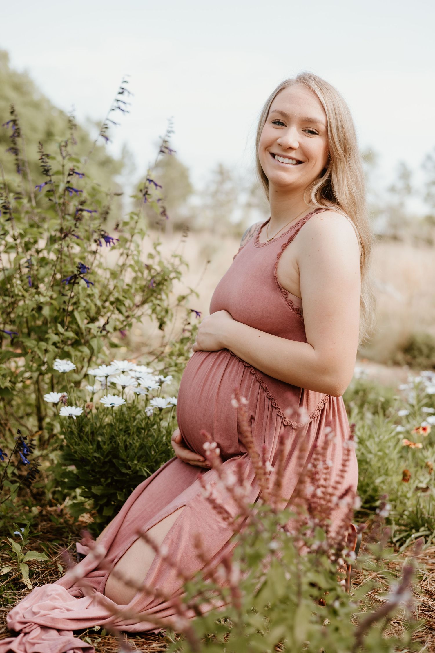 A glowing maternity photo session in a wildflower meadow featuring a dusty rose dress and natural outdoor scenery.