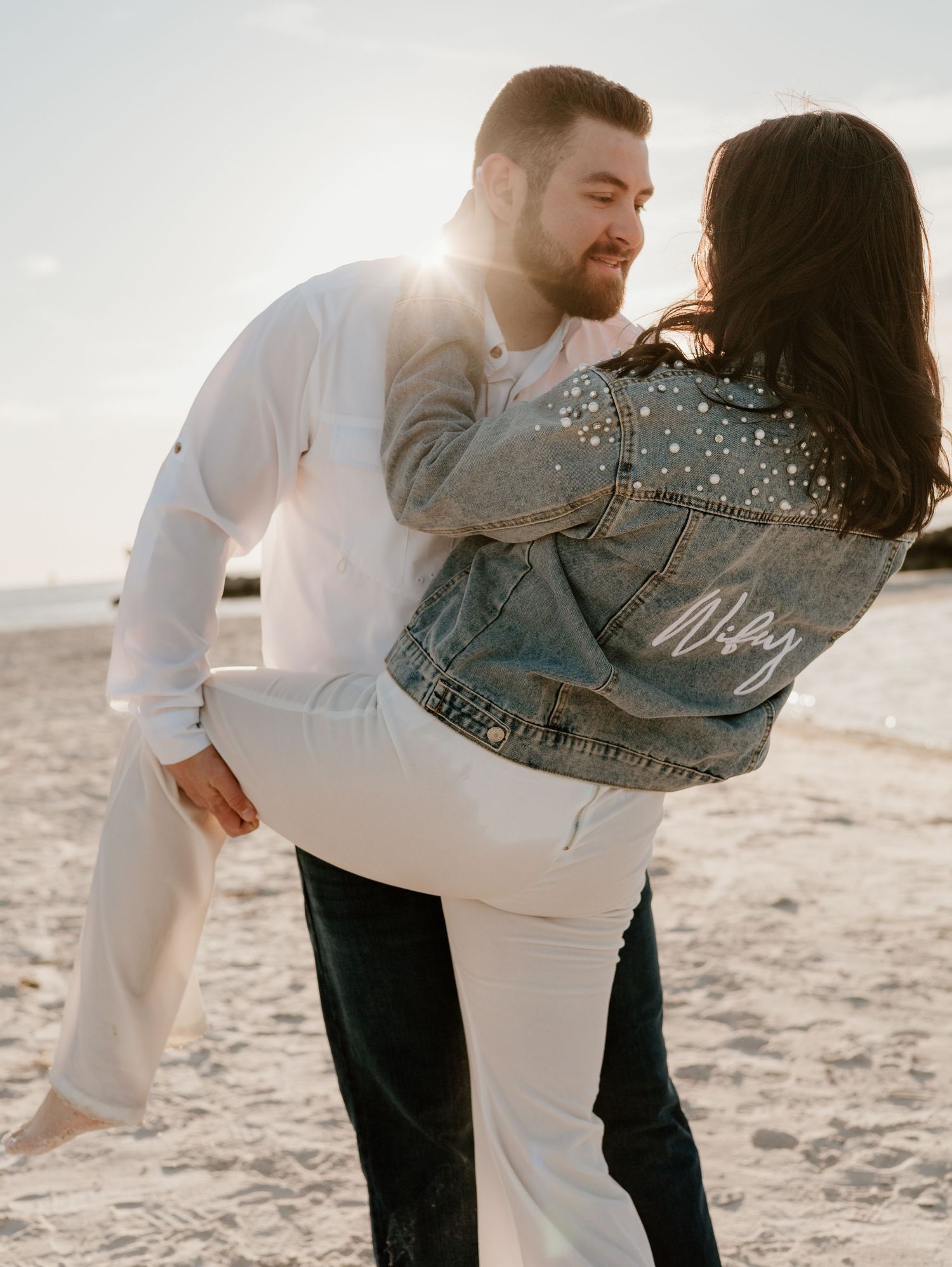 Romantic couple dancing and twirling together on a sunlit beach at sunset.