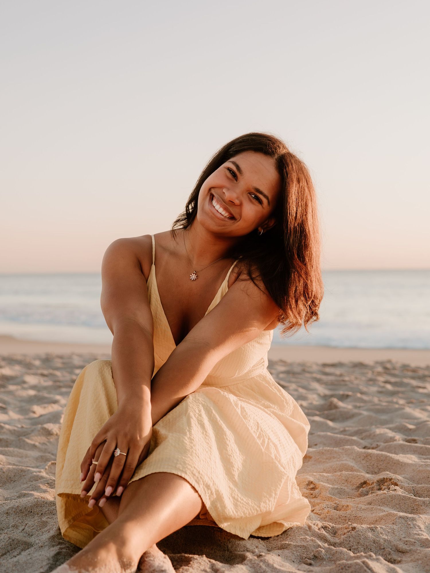 Woman in yellow dress sitting on beach sand during golden hour.