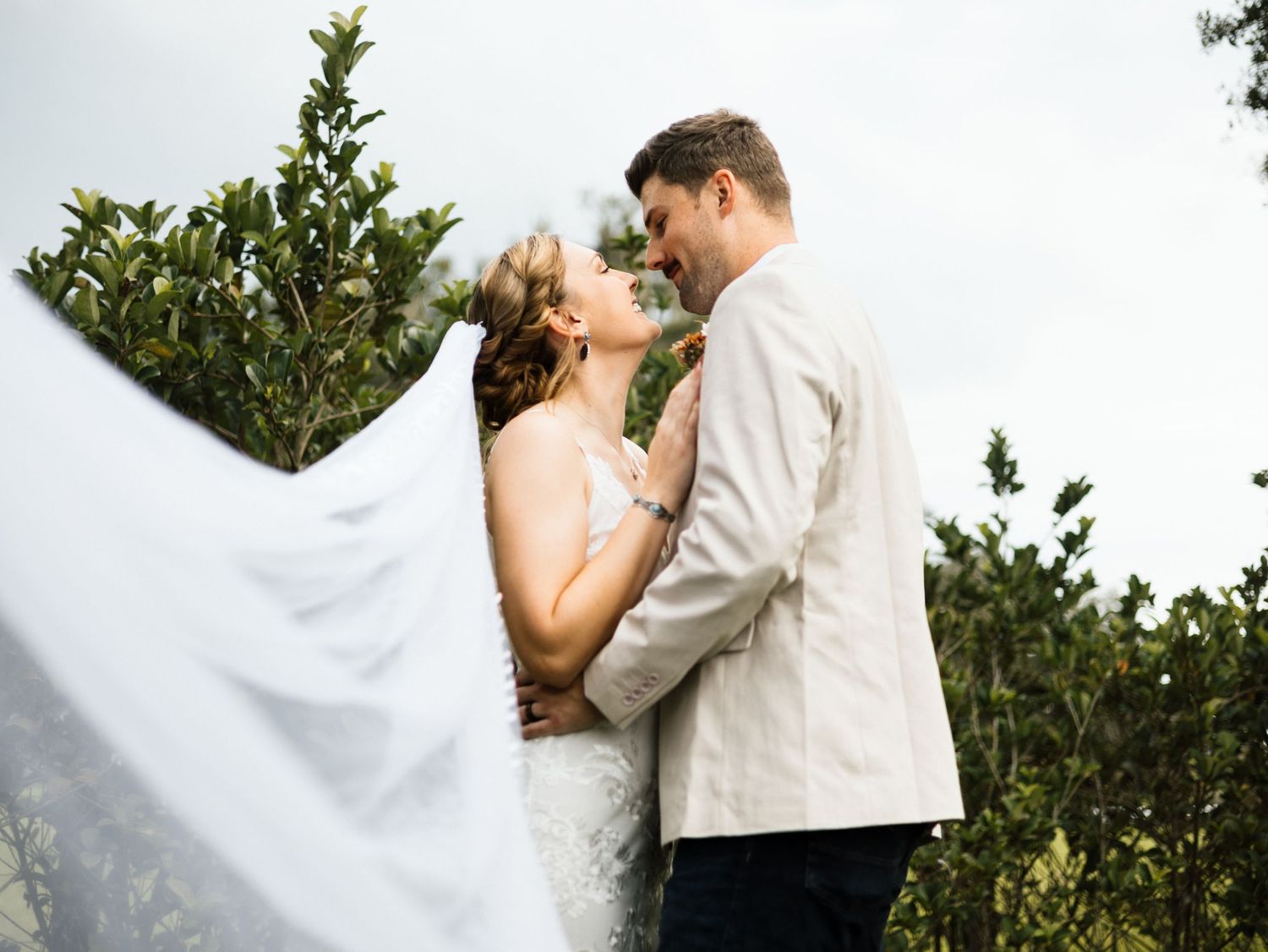 A couple shares an intimate kiss in front of lush greenery during an outdoor wedding ceremony.