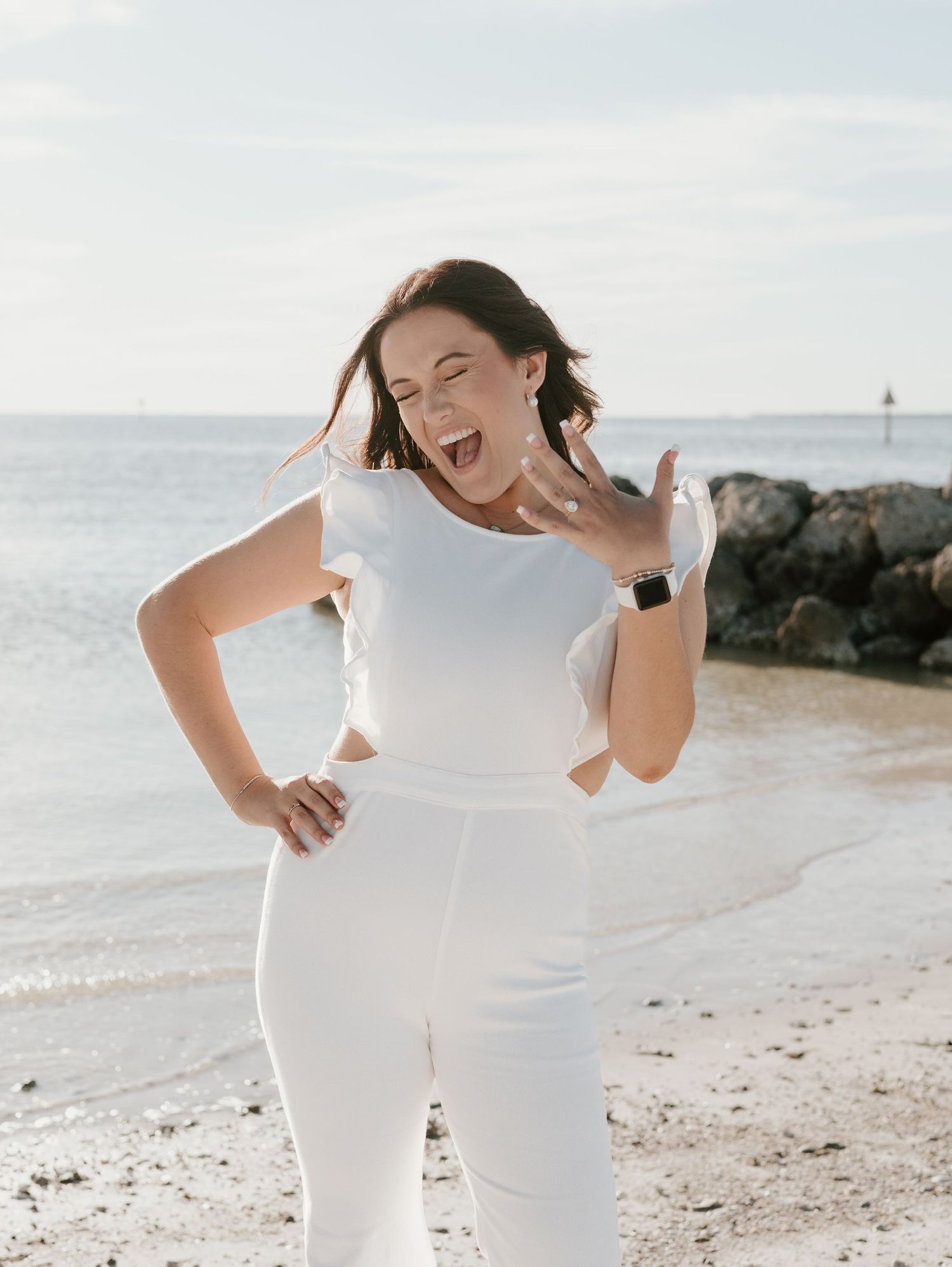 Person in white outfit expressing joy and excitement on a sunny beach.
