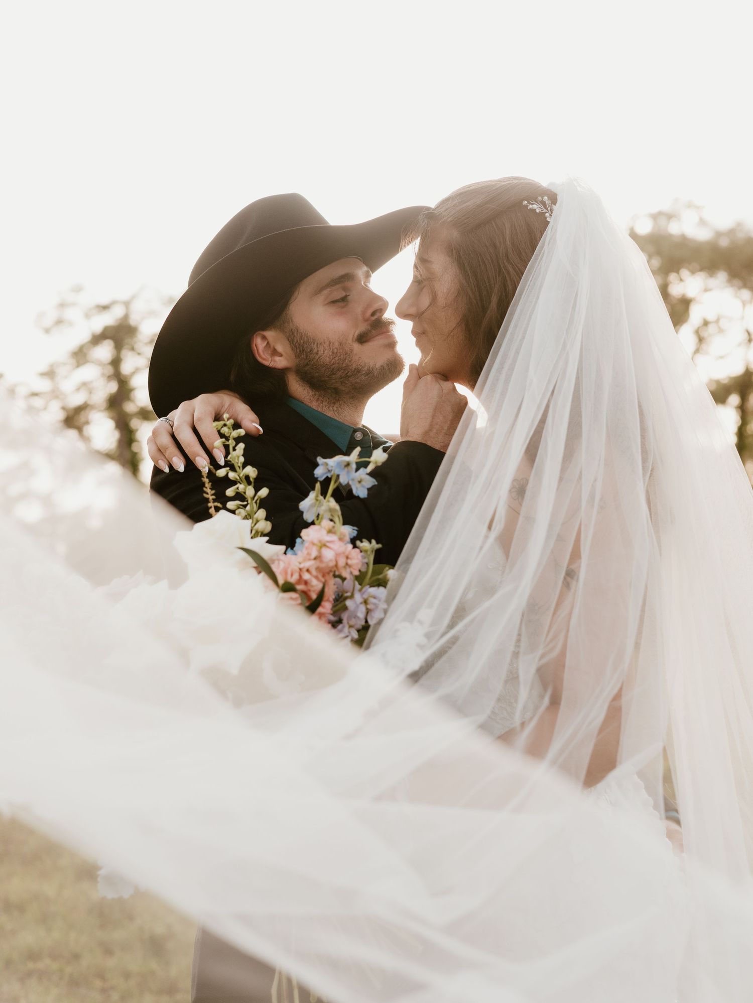 A romantic wedding couple shares intimate moment in golden sunlight as white veil flows gracefully in the breeze.