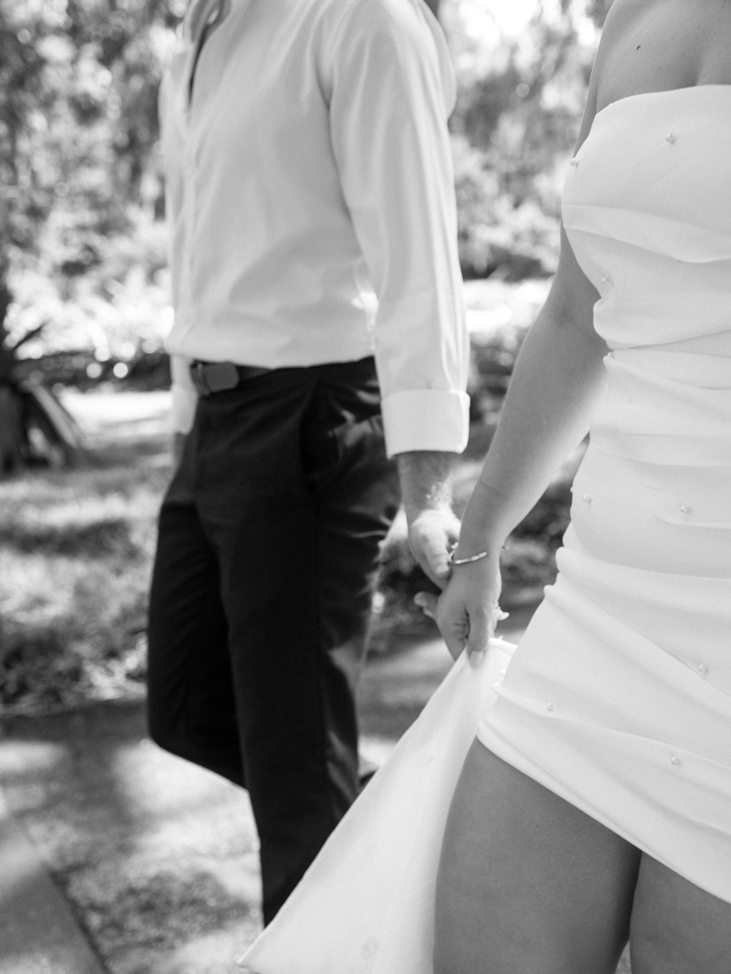 Close up detail of a white wedding dress with a person wearing black pants standing in a blurred background.
