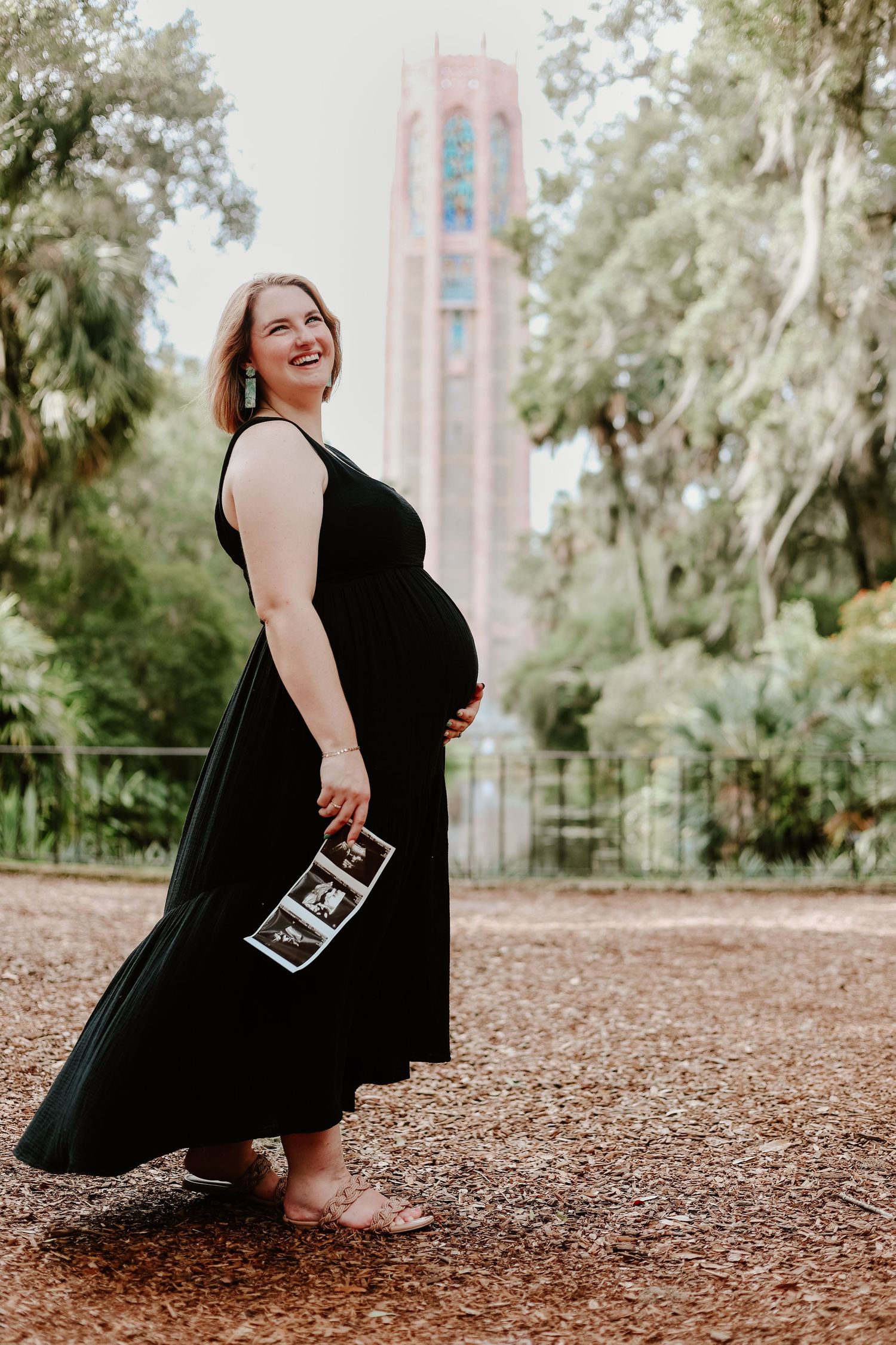 Maternity photoshoot in black dress holding ultrasound photos near brick building.