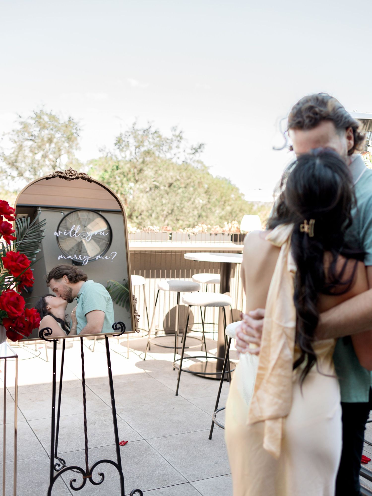 A decorative easel displays a framed photograph with red floral arrangements at an outdoor terrace event.