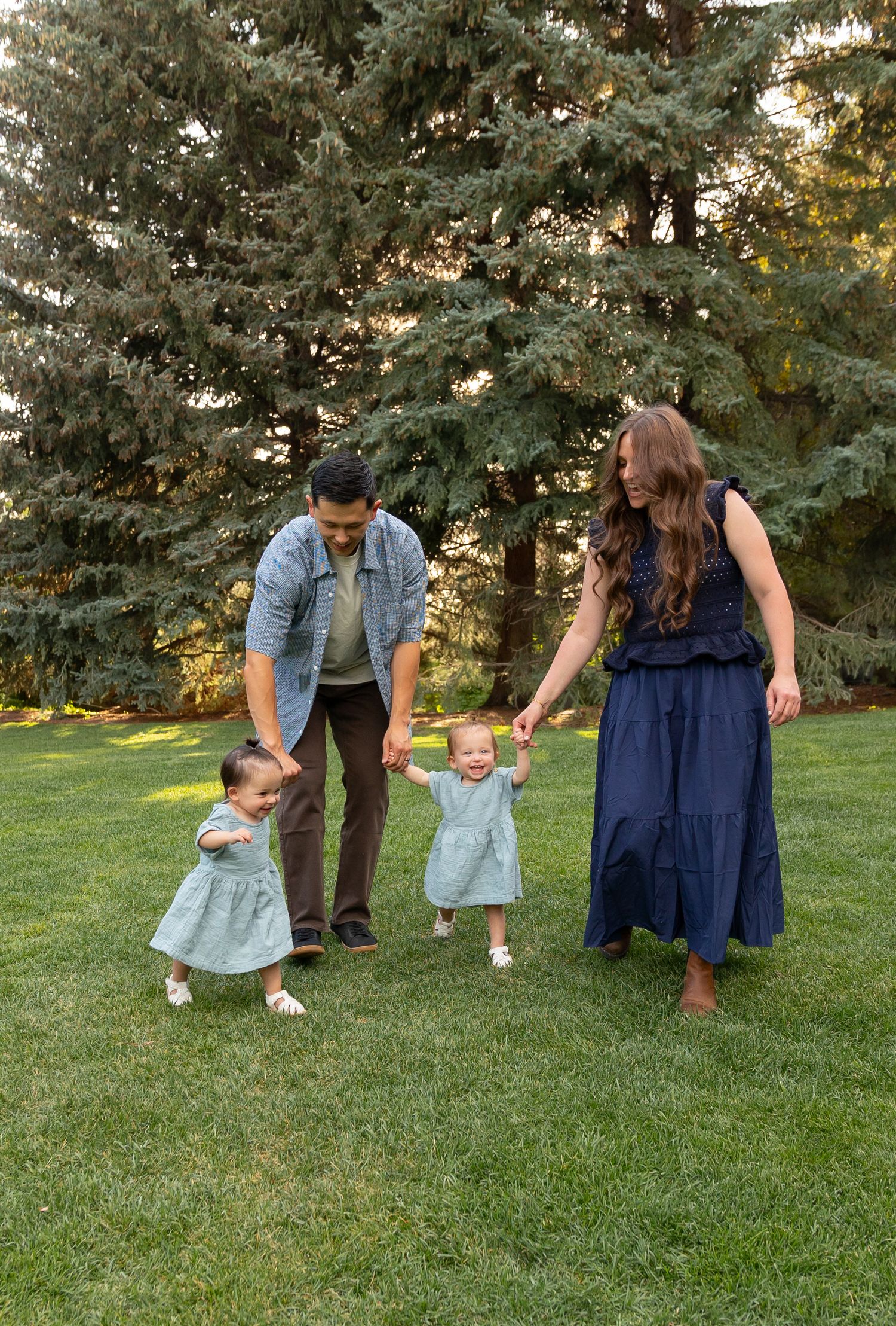 Family photo of a young mother and father with two twin toddlers in a green field