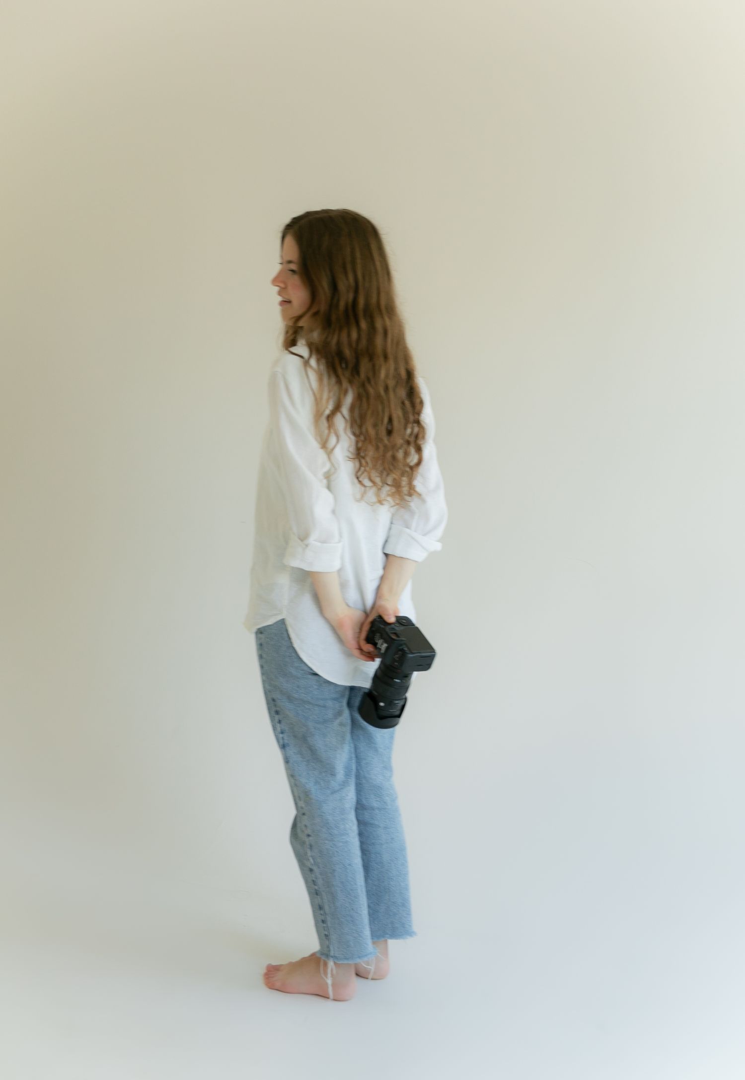 A woman holding her camera in front of a white wall