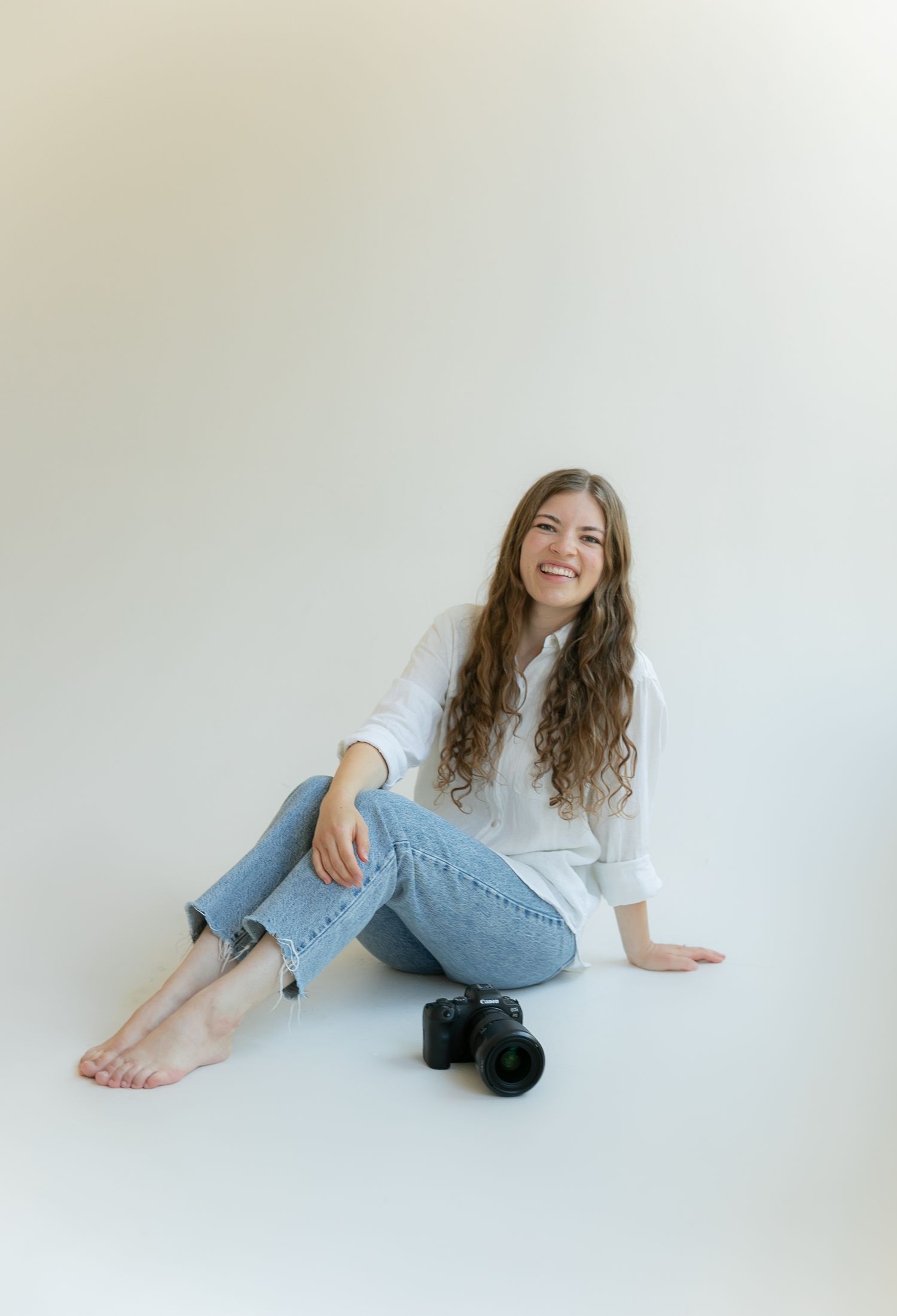 A woman sitting next to a camera in a white room