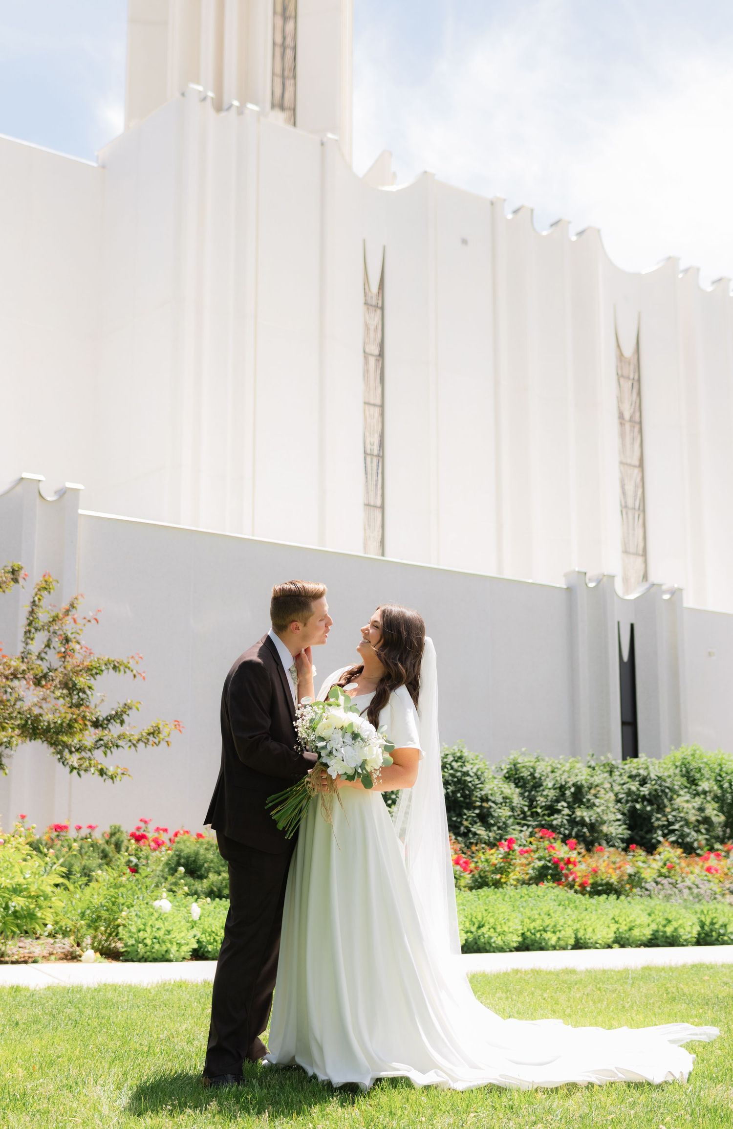 A bride and groom standing outside the Jordan River Utah Temple