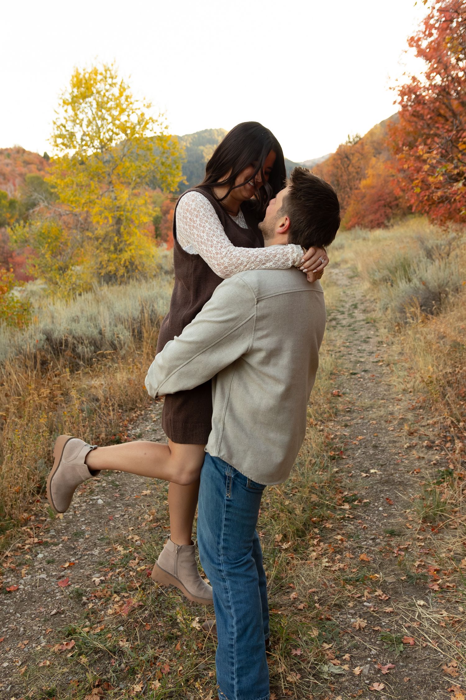 A man holding up his wife in front of fall leaves