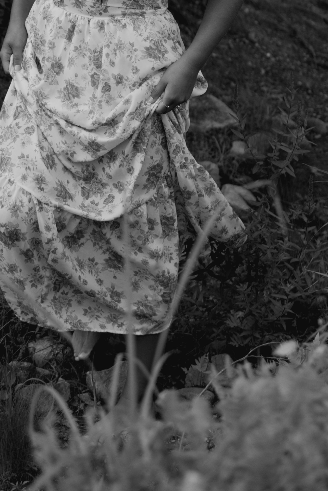 Someone wearing a floral pattern dress sits in tall grass, creating a dreamy black and white composition.
