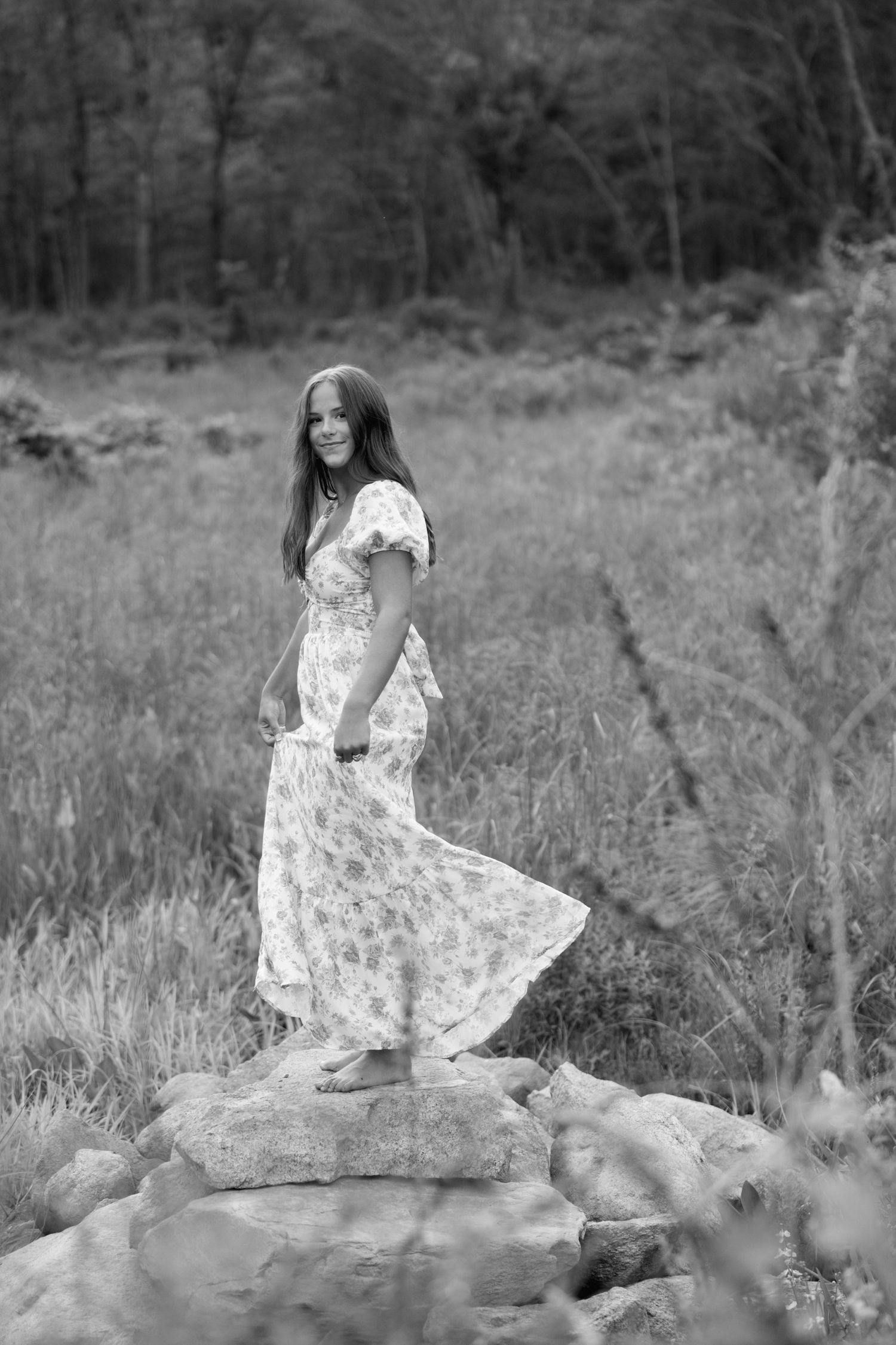 A flowing white floral dress creates an ethereal effect against a misty natural outdoor backdrop in black and white photography for senior.