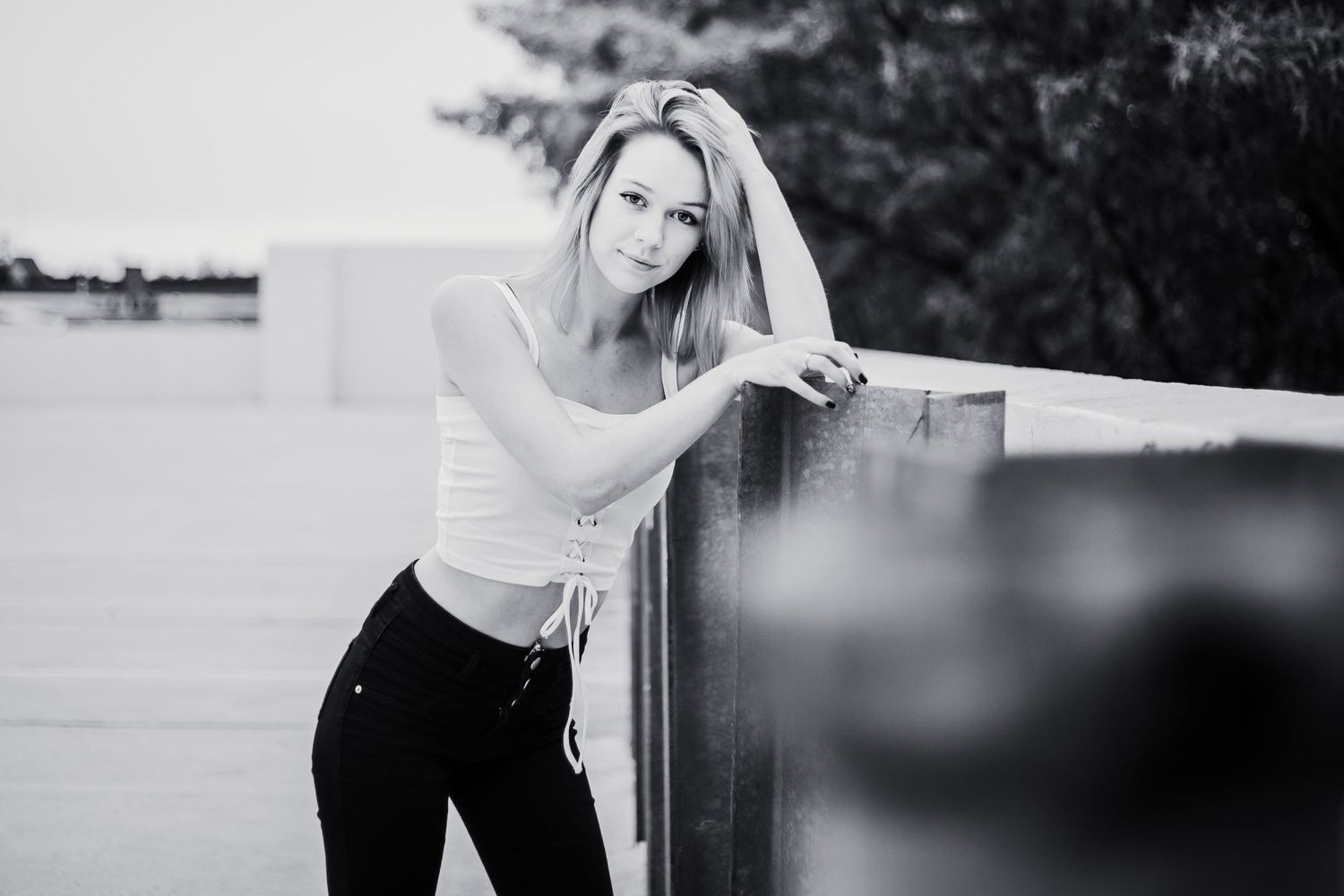 Black and white portrait of high school senior posing casually against a railing outdoors in casual attire in keene, new hampshire