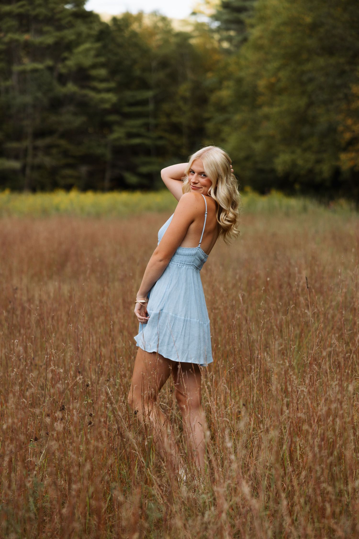 Dancing in a light blue dress through a golden autumn field under a thick forest canopy in senior photoshoot in Keene, New Hampshire
