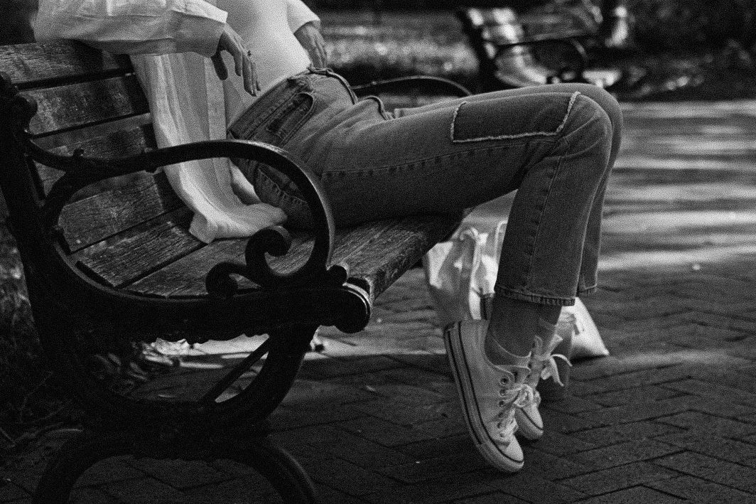 Wearing jeans and sneakers sitting casually on a park bench in a black and white photograph during a NH senior portrait session.