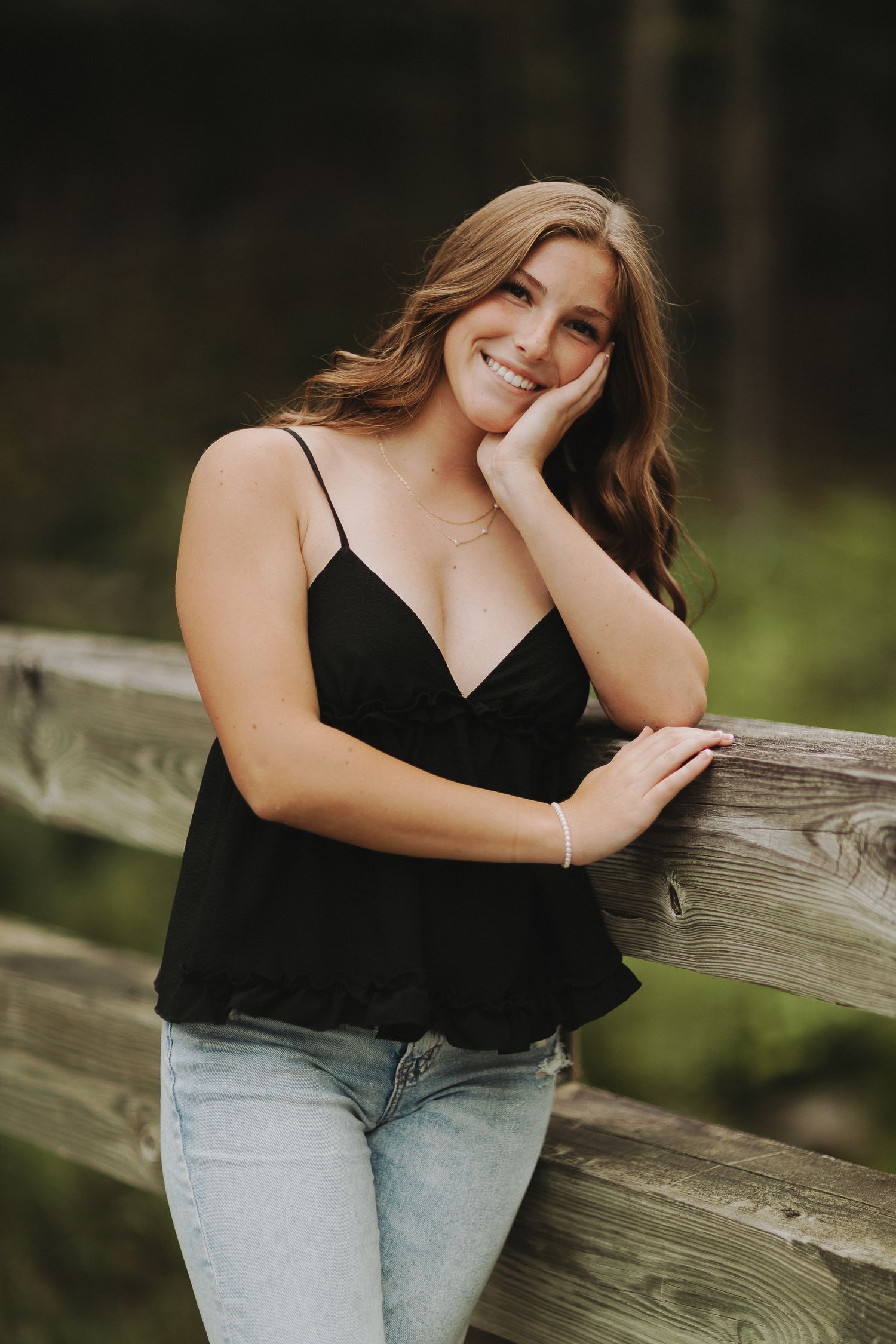 A series of casual outdoor portrait poses capturing a girl in a black top and jeans leaning on a rustic wooden fence in Otter Brook Park