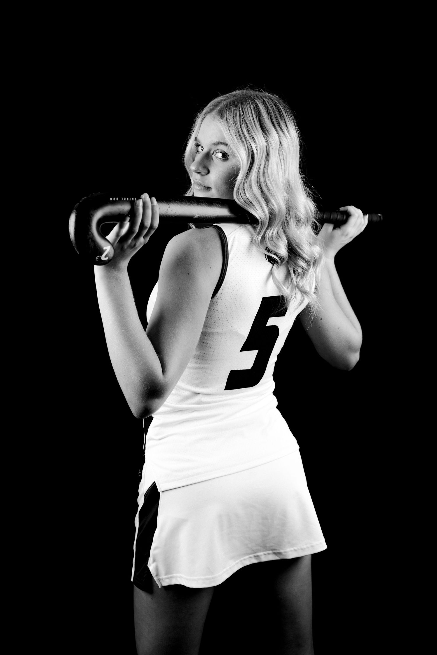 Black and white artistic photo series showing a field hockey girl posing with dynamic movement against dark background for studio photos.