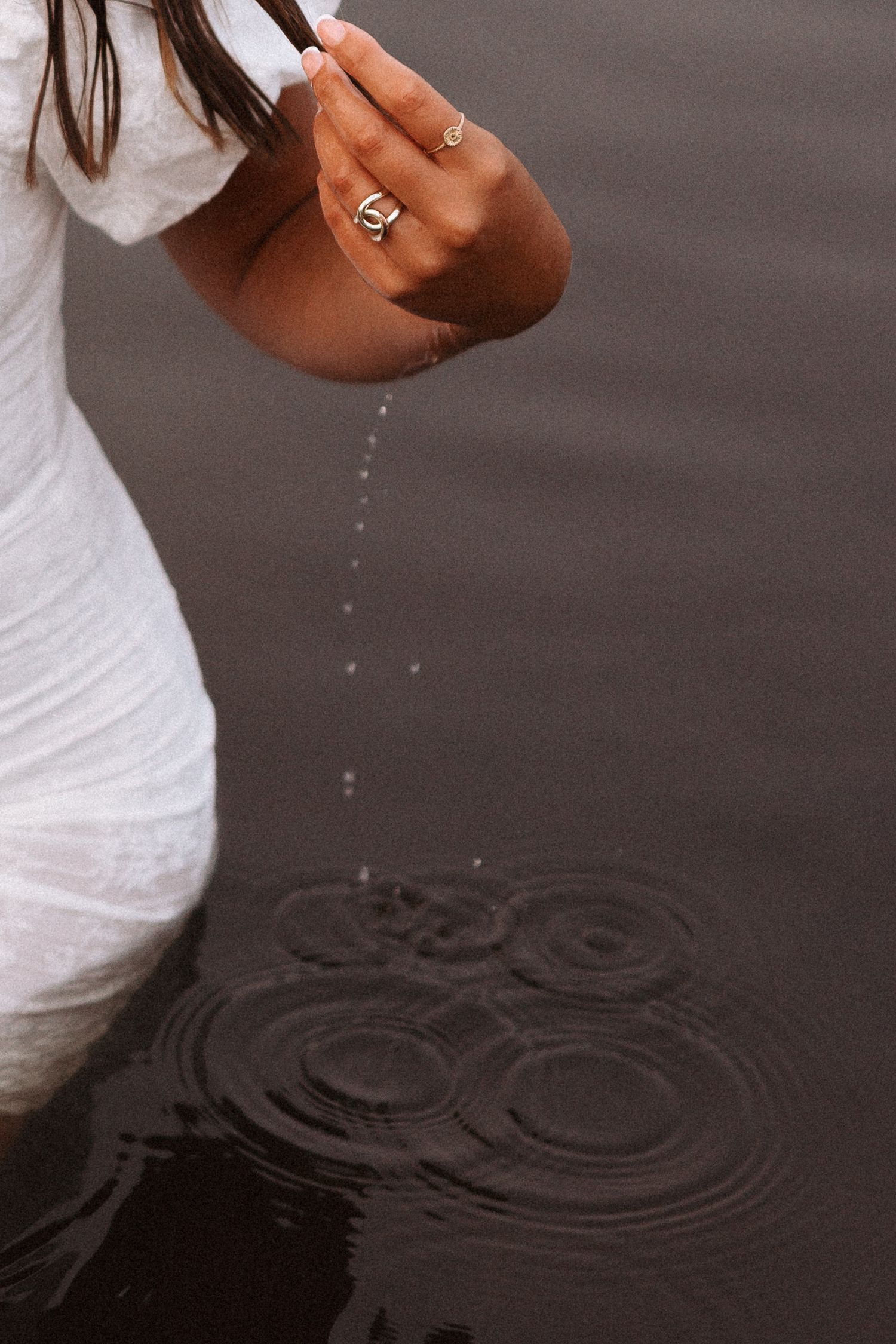A hand draws rippling patterns by moving fingers through dark water on a reflective black surface Keene, New Hampshire