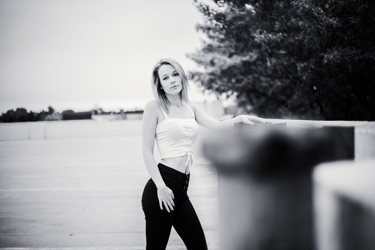 Black and white portrait of high school senior posing casually against a railing outdoors in casual attire in keene, new hampshire