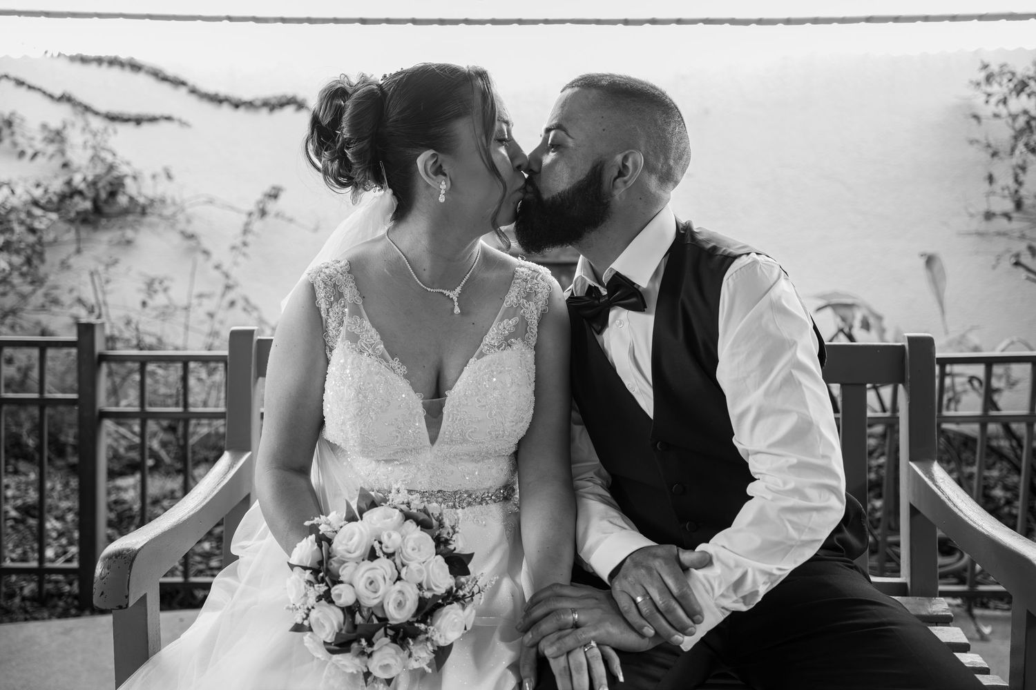 Black and white photo of a bearded groom kissing his bride on the cheek at their wedding reception.