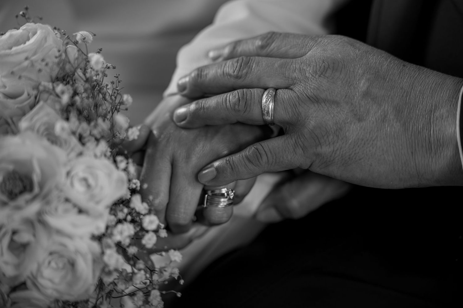 Close-up of bride and groom hands with wedding rings resting on a bouquet of roses.
