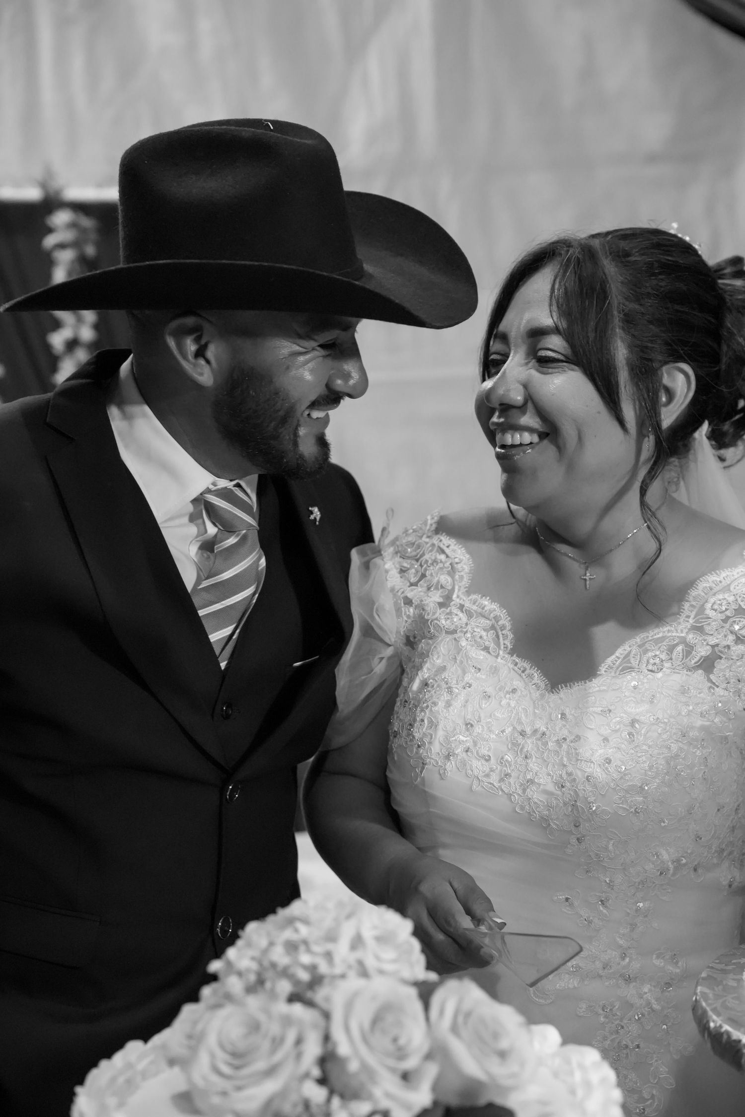 Black and white photo of smiling bride and groom in cowboy hat at wedding reception.