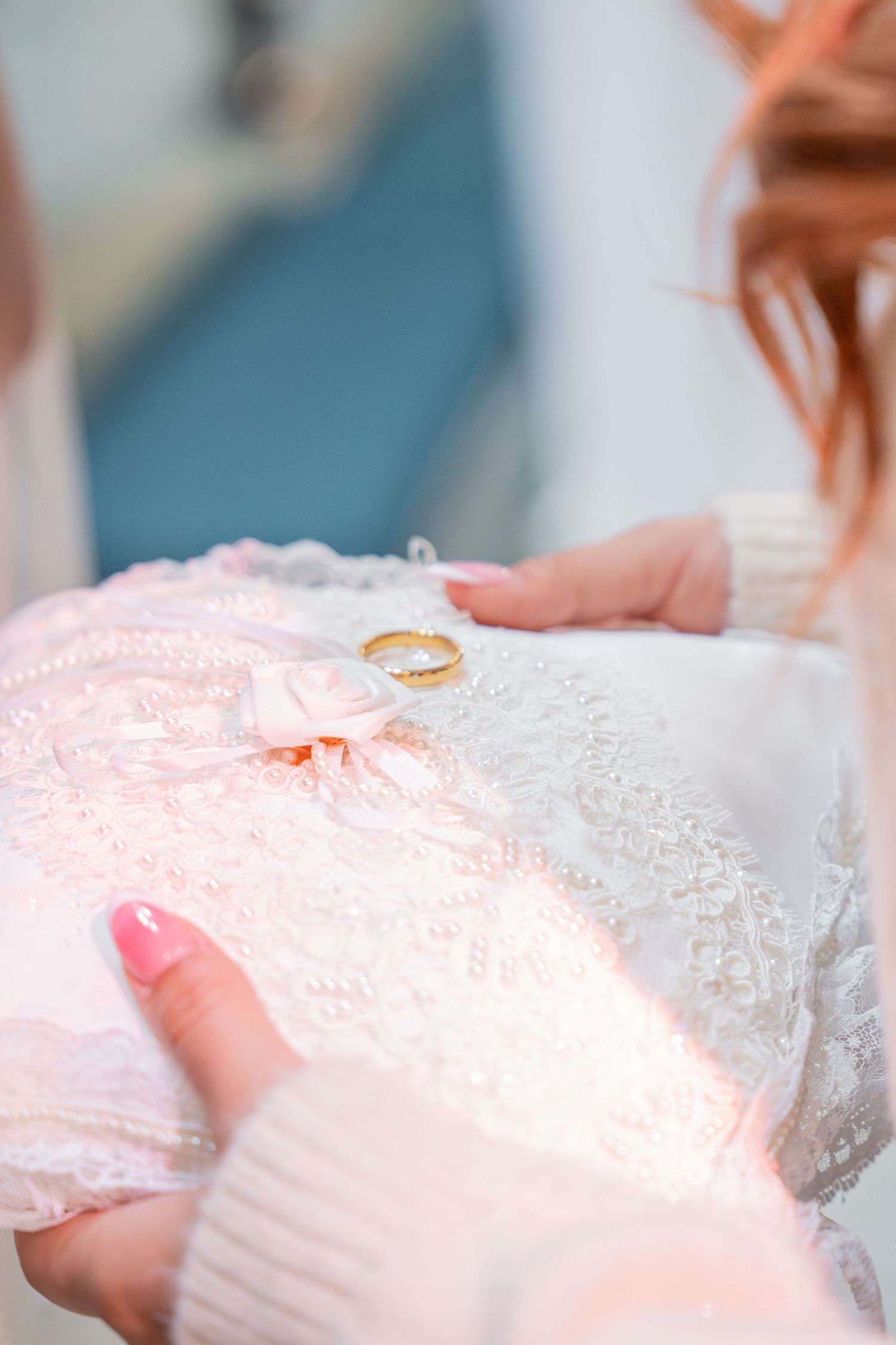 Close-up of a gold wedding ring resting on a decorative white lace ring bearer pillow.