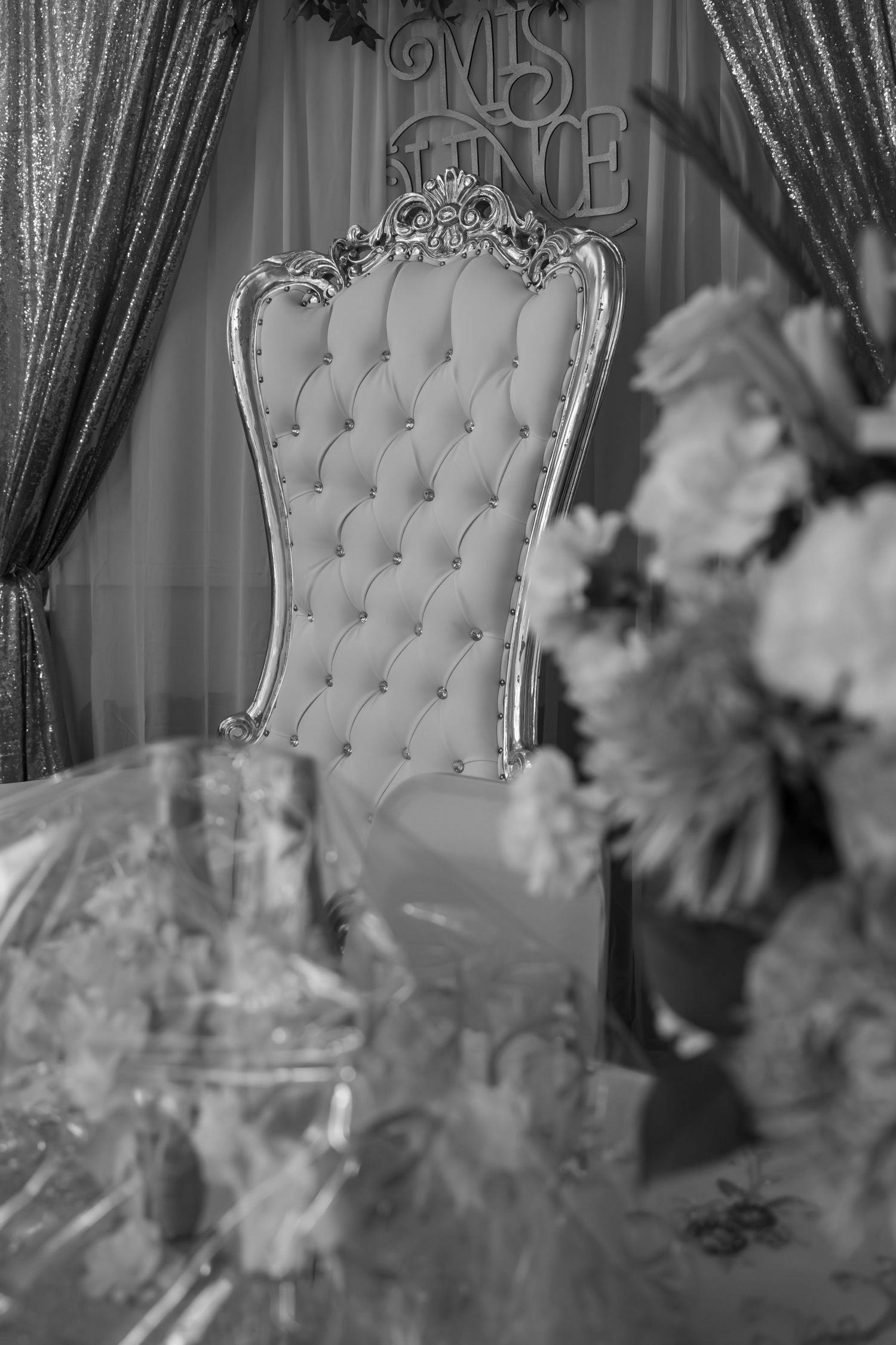 Black and white photo of ornate tufted throne chair at quinceañera celebration with floral decor.