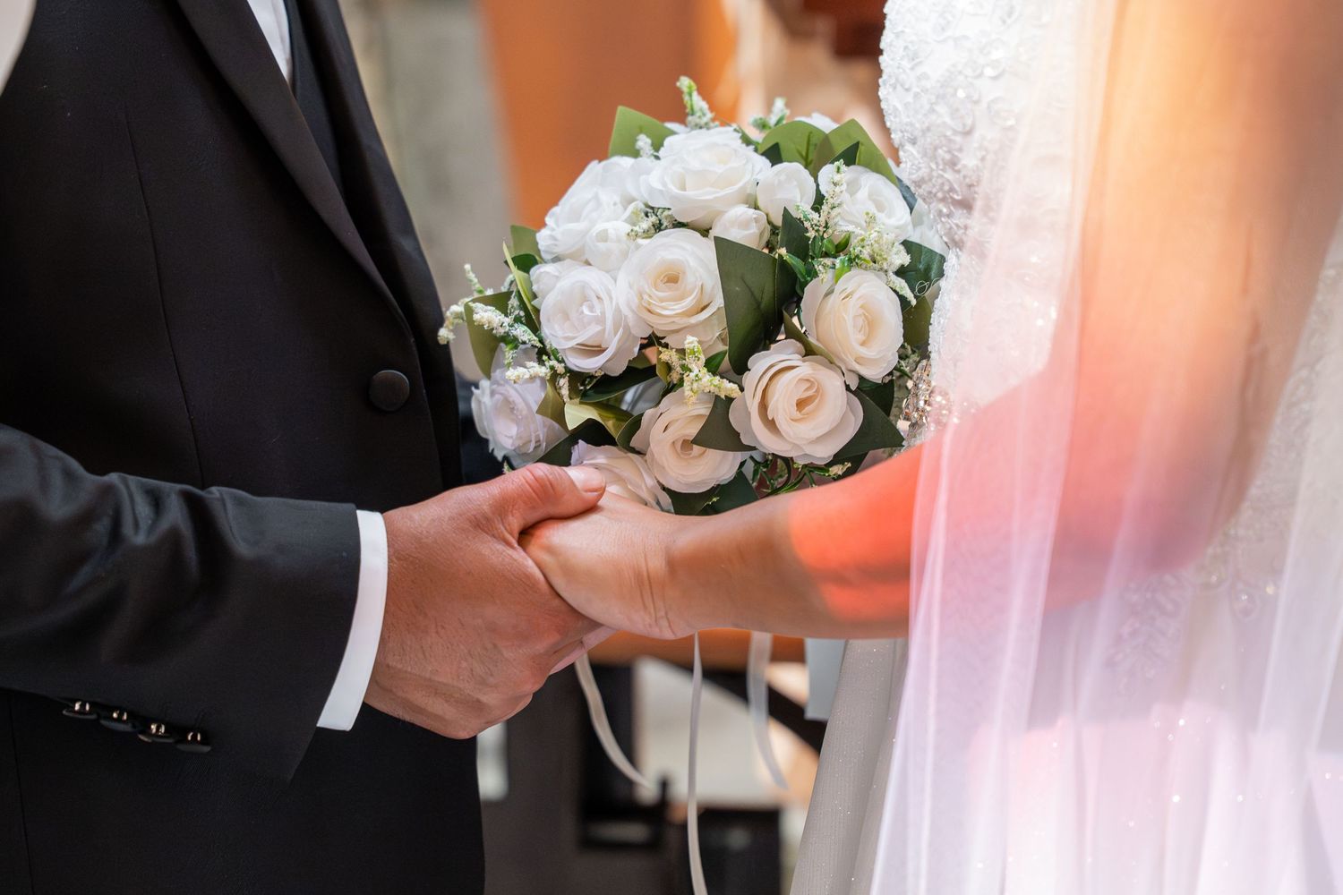 Bride and groom holding hands with a beautiful white rose bouquet during their wedding ceremony.