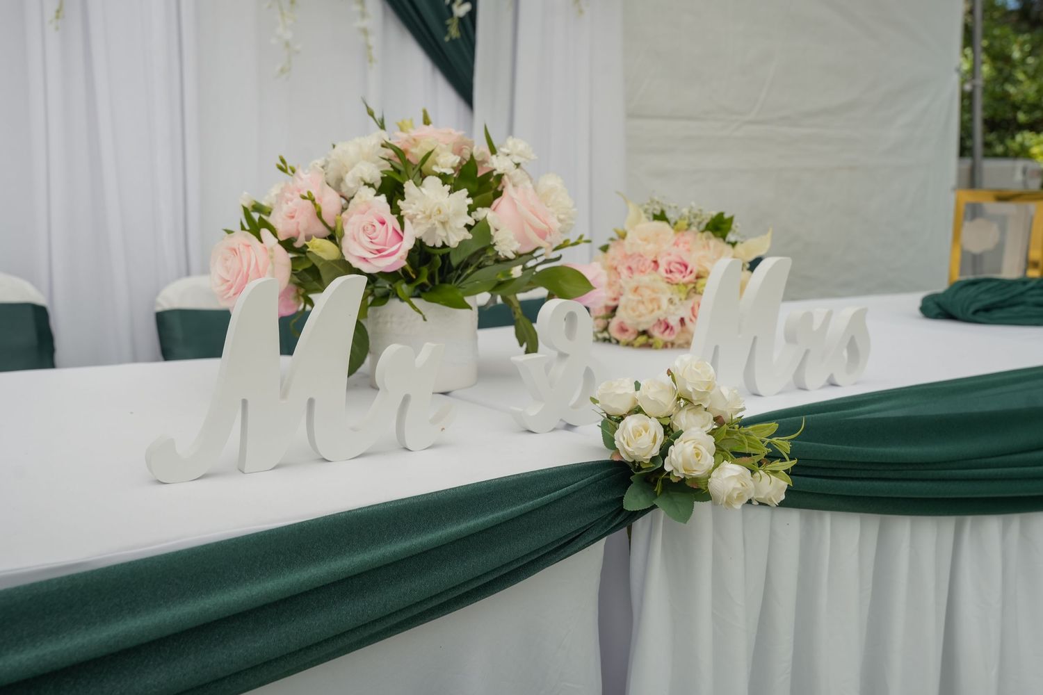 Mr and Mrs wedding reception head table decorated with pink roses and green satin fabric draping.