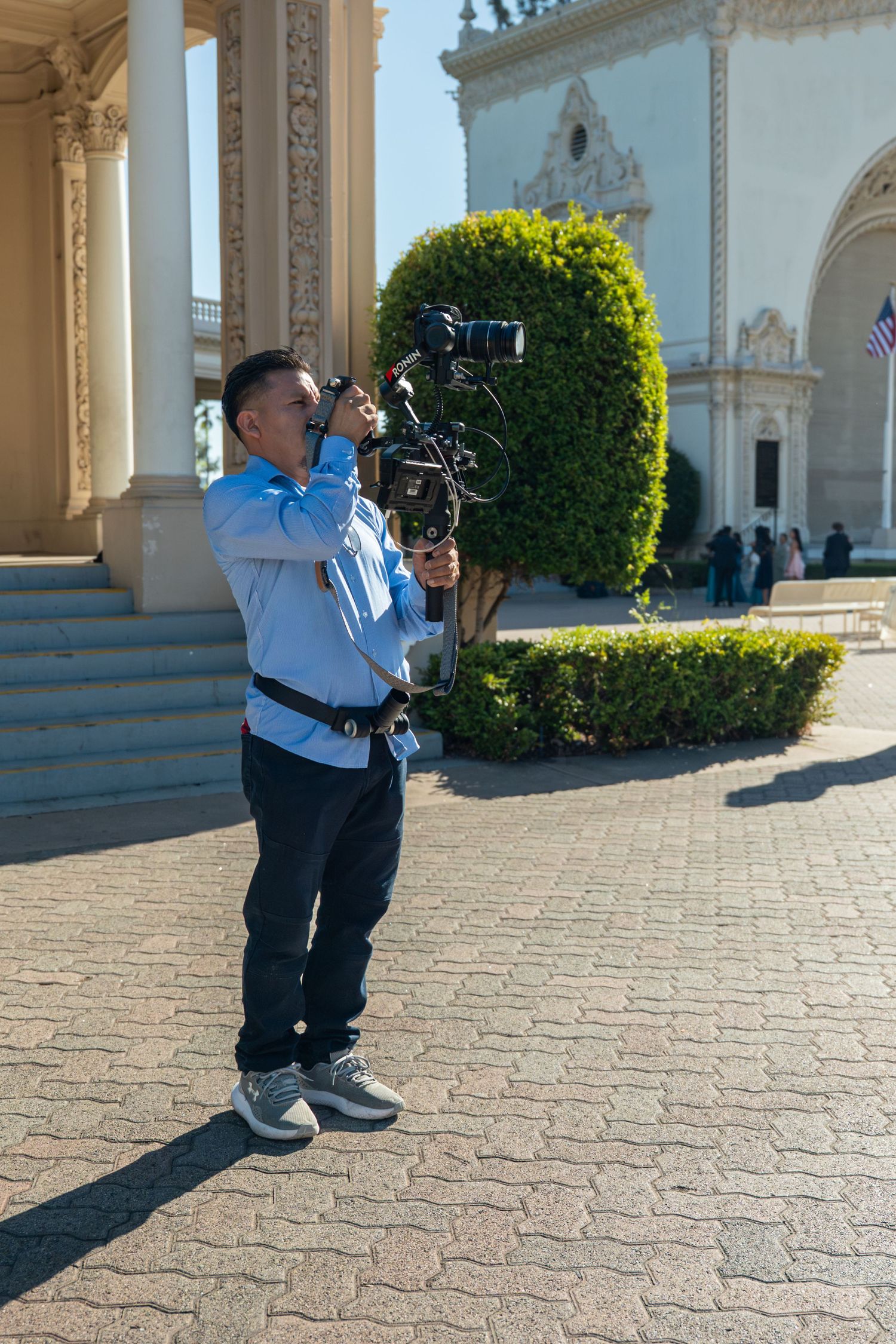 Professional videographer using a gimbal stabilizer to film at a beautiful outdoor wedding venue.
