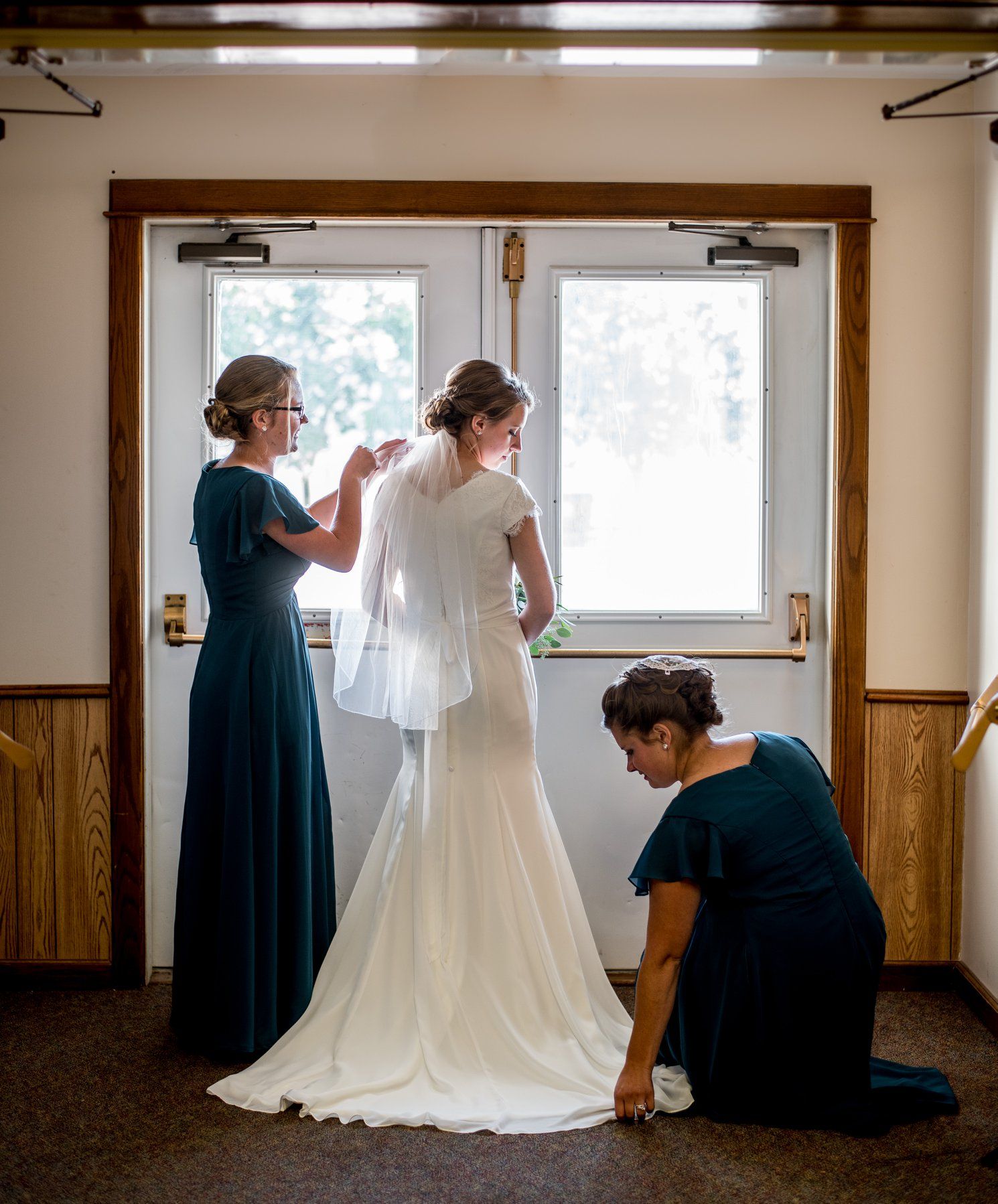 Wedding dress preparations shown in a wood-paneled dressing room with natural light.