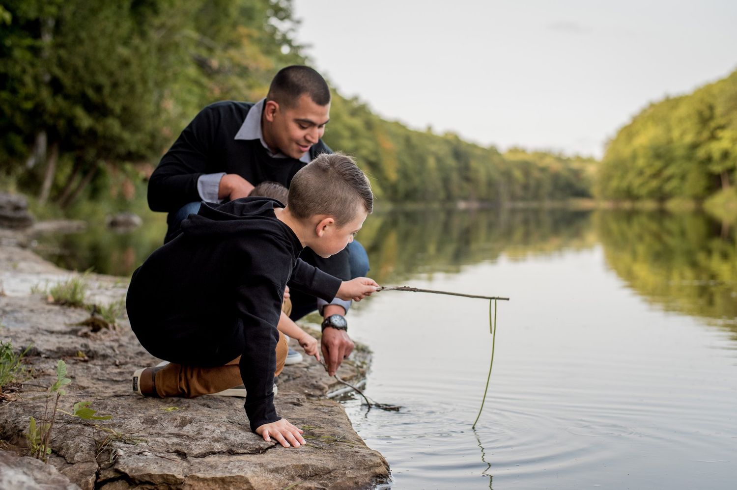 Someone fishing with a rod at the edge of a peaceful lake during daytime.
