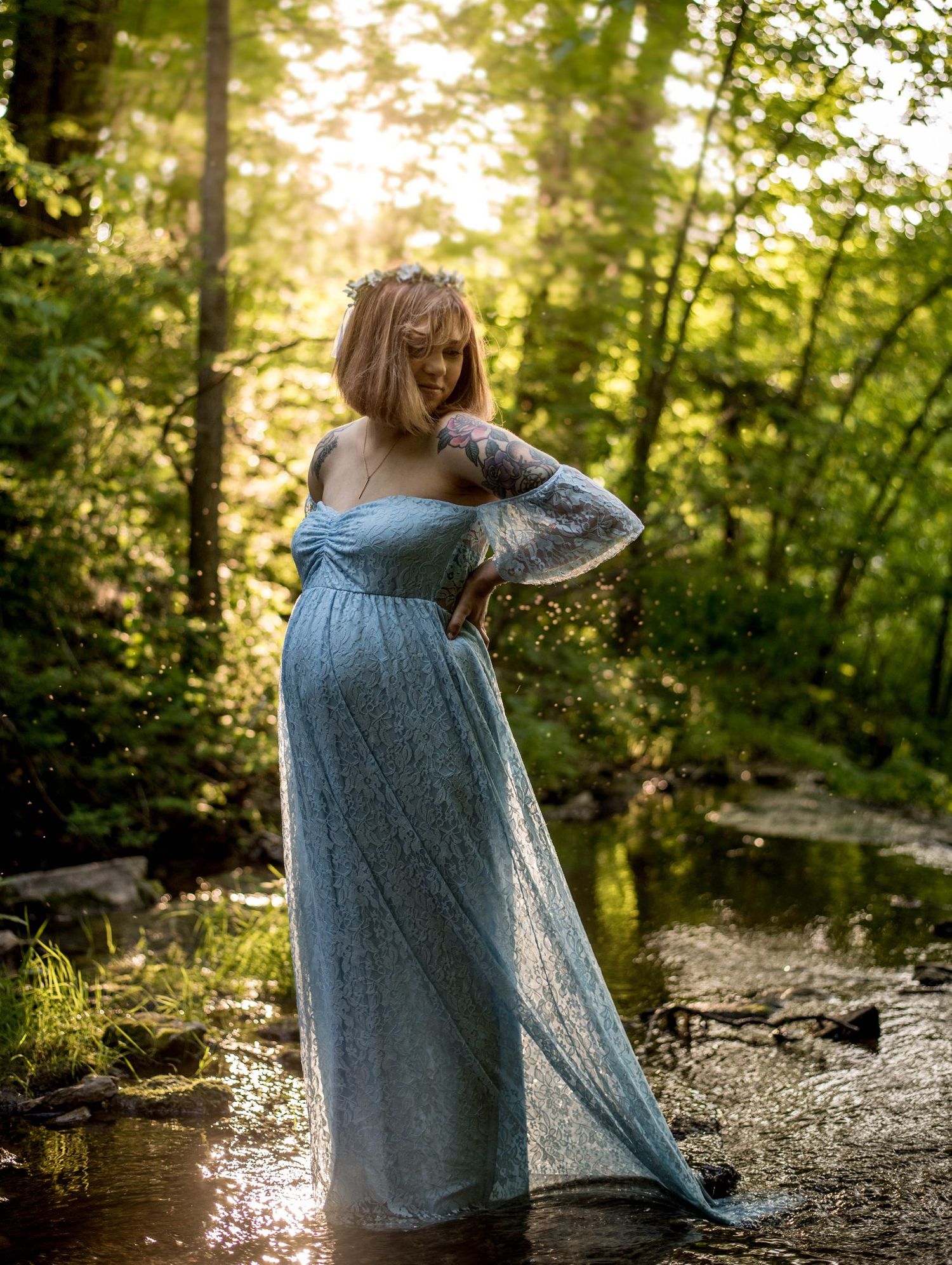 Artistic portrait session by a stream with sunlight filtering through trees.