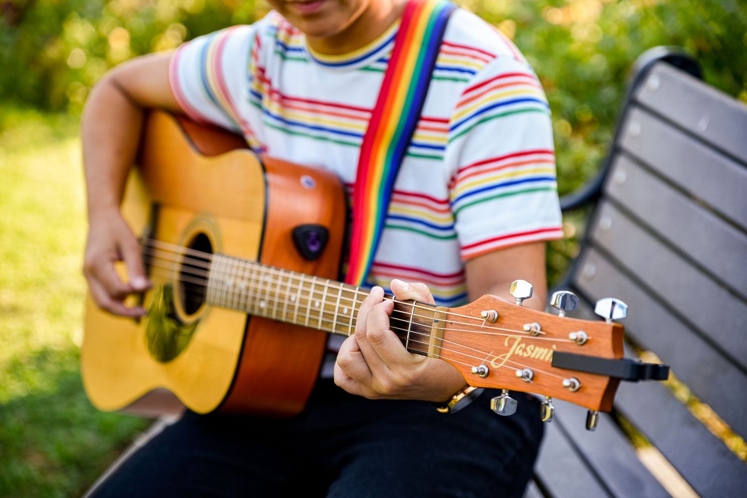 Person playing colorful striped acoustic guitar outdoors in sunlight.