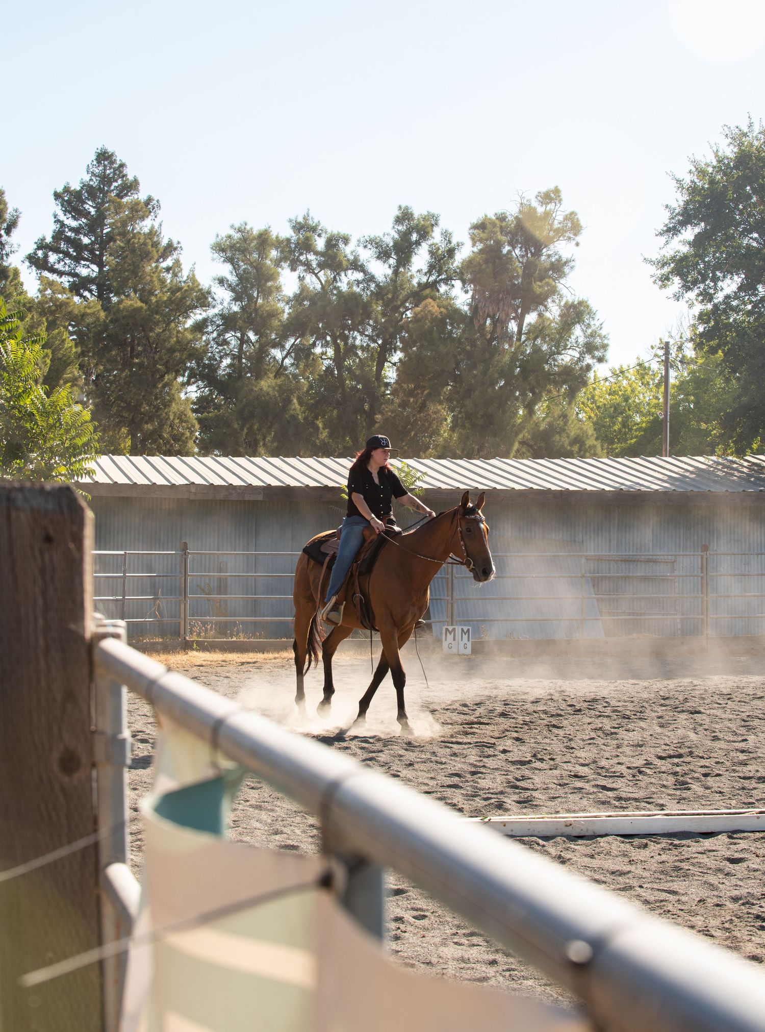 Horse and rider practicing in a dusty riding arena with metal fencing visible.