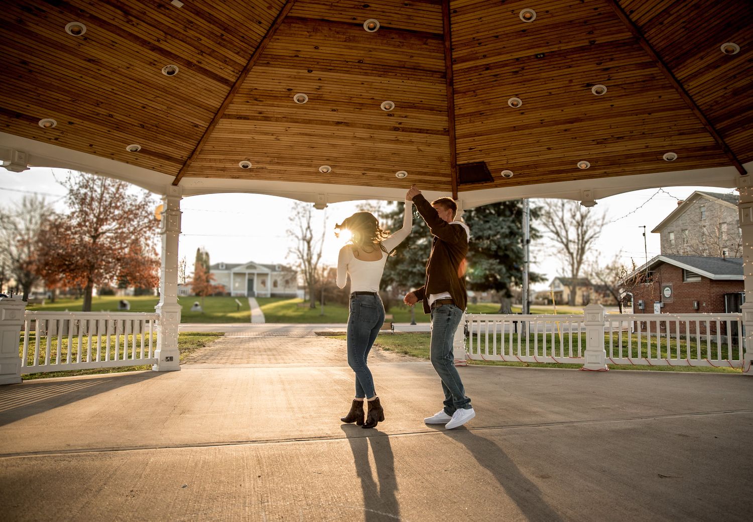 Skateboarders practice tricks at a wooden skate park during golden hour sunset.