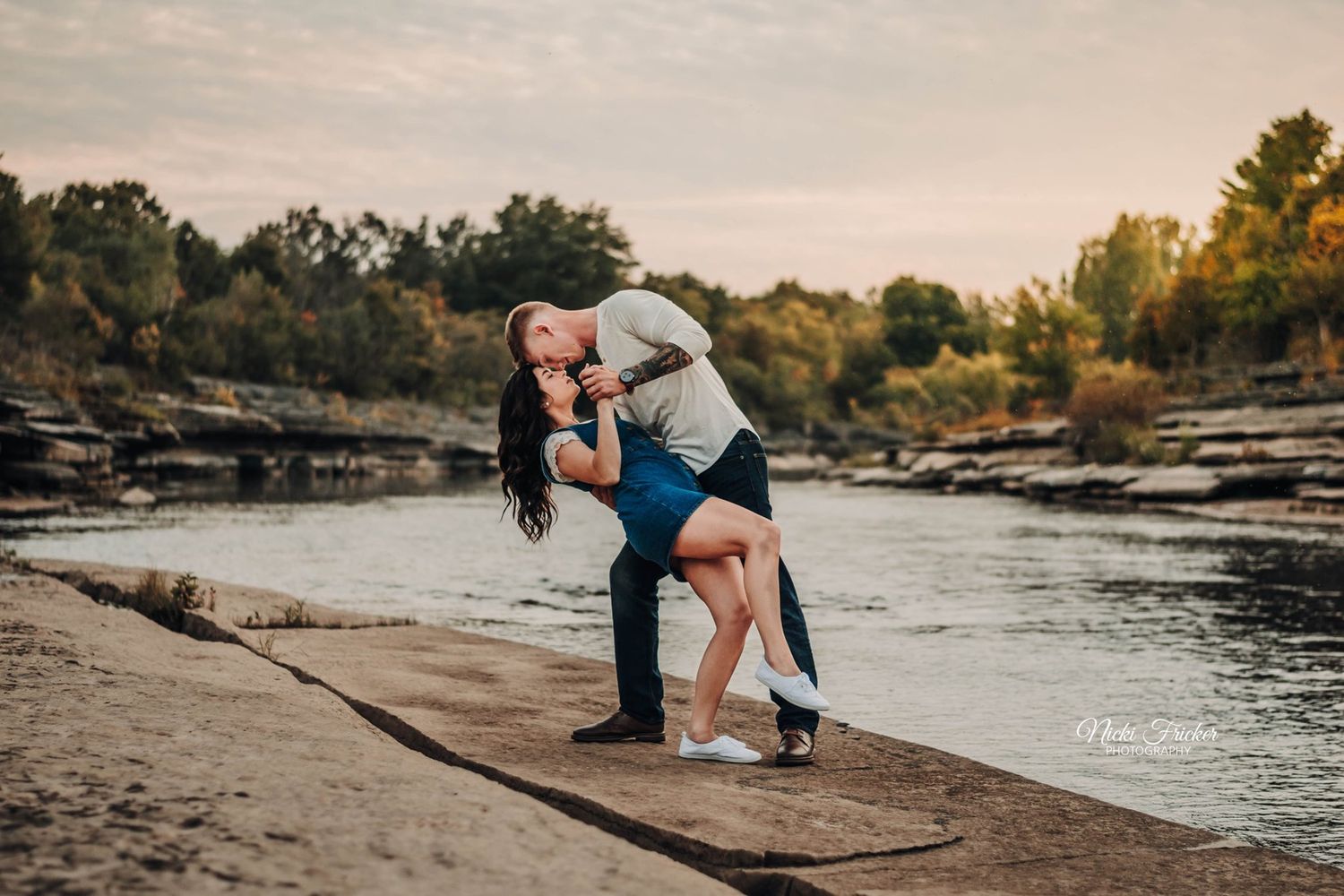 Romantic engagement session along rocky riverbank at golden hour.