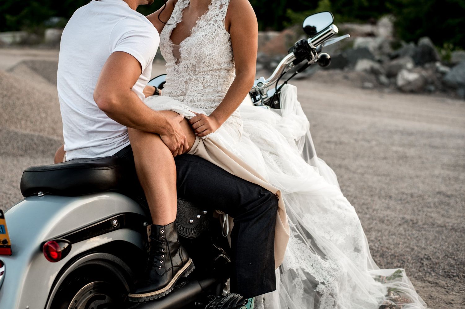 A couple posing with a motorcycle in casual wedding attire.