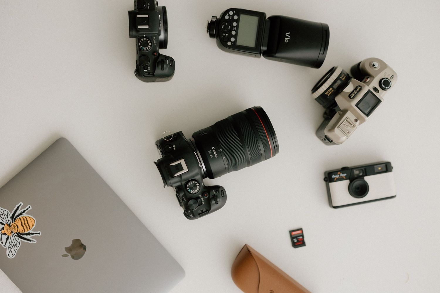 Flatlay of professional camera equipment and a MacBook with bee sticker on white background.