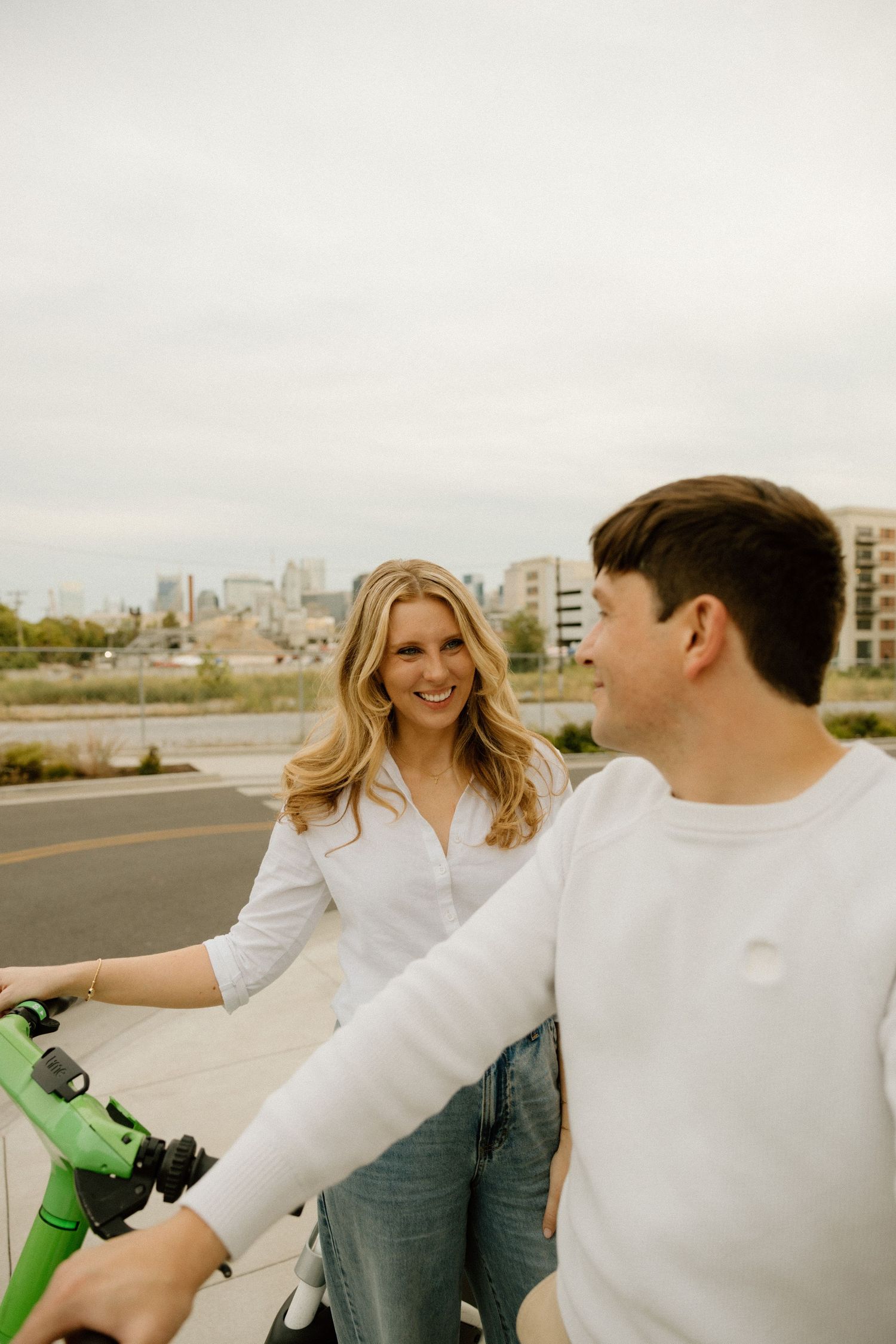 Couple in white clothing sharing a playful moment while riding bikes outdoors.