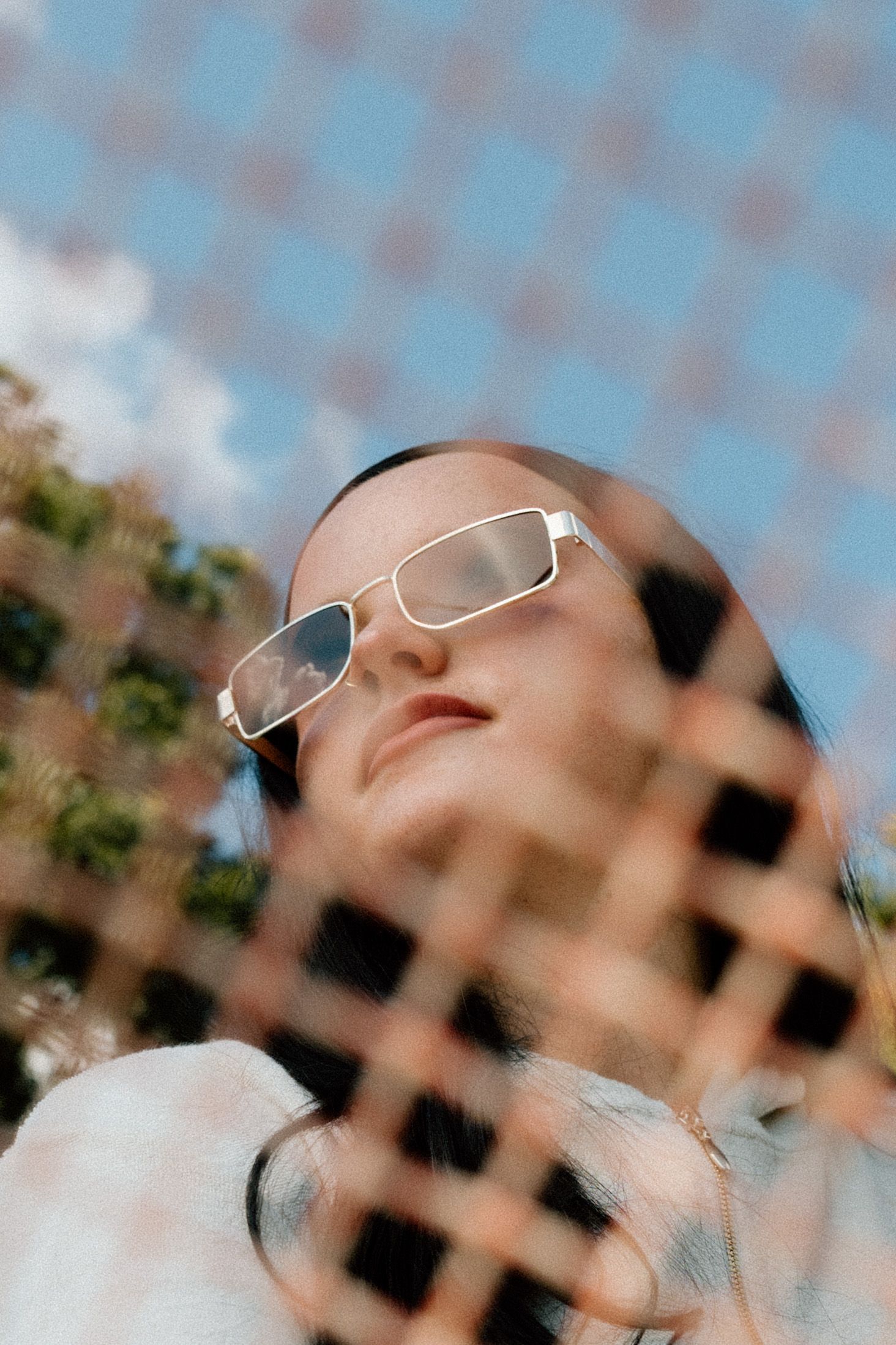 Abstract portrait through a grid pattern showing white-framed sunglasses against a blue sky.