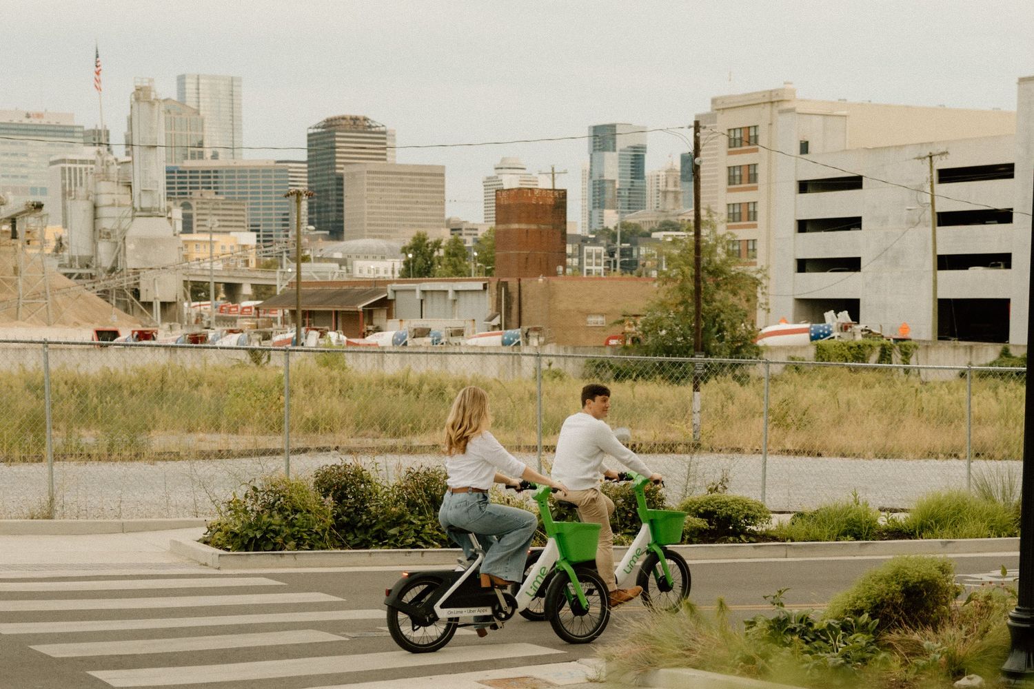 Two people riding green bikes through an urban landscape with city buildings in the background.