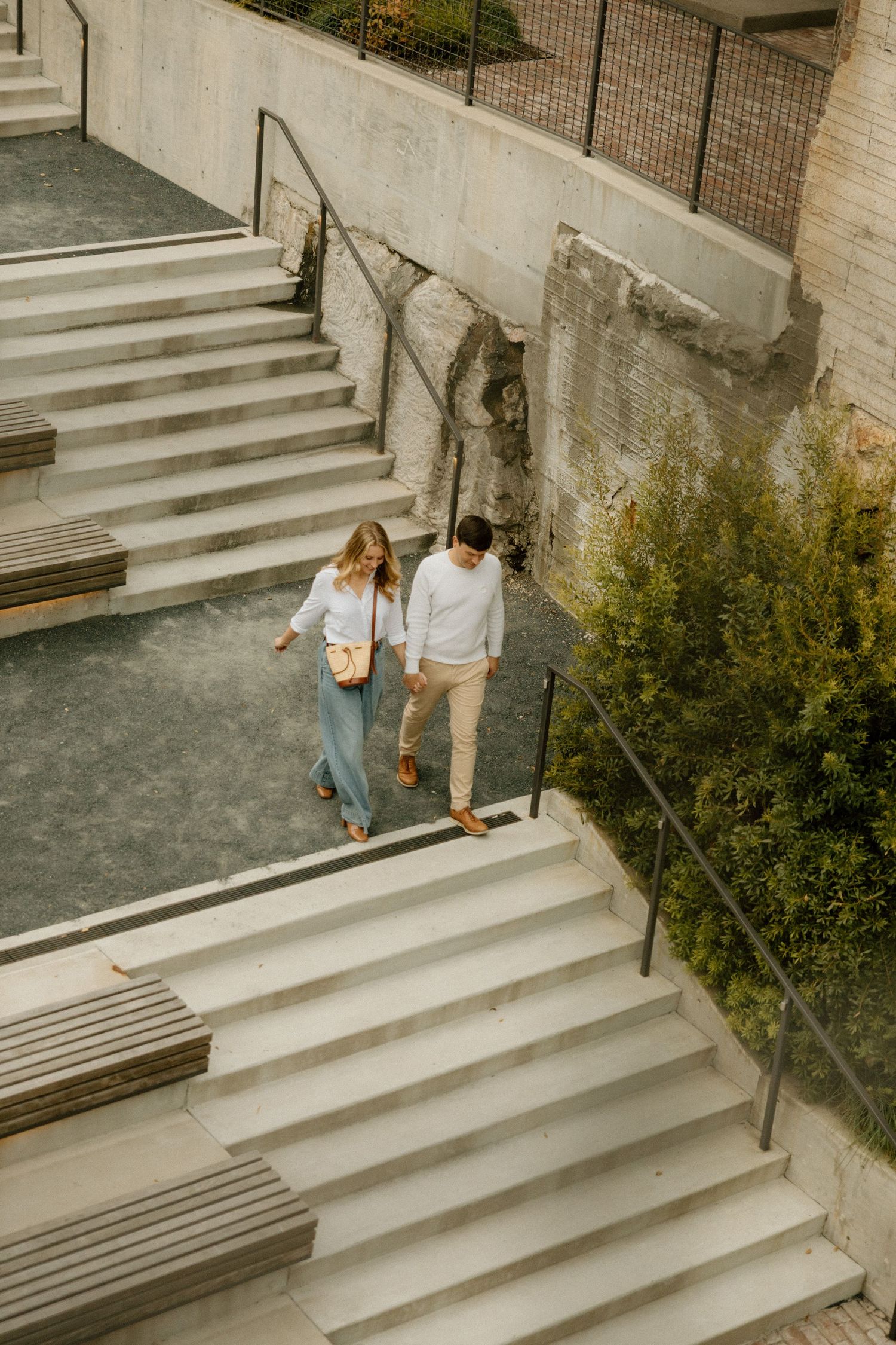 Two people walk down concrete steps surrounded by greenery.