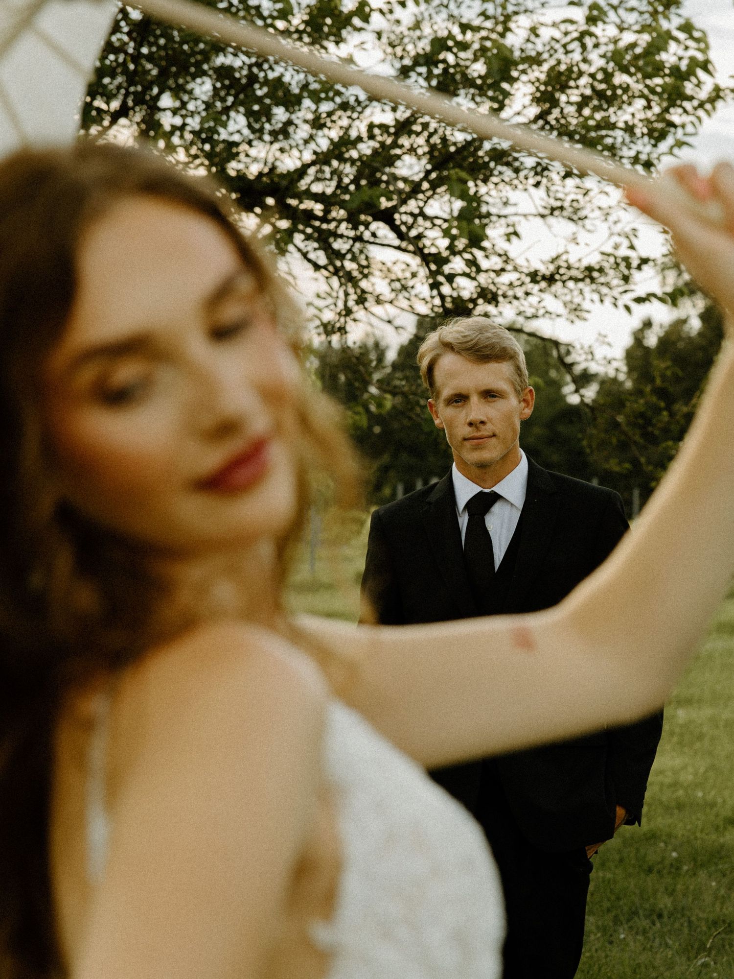 A romantic wedding photo captured through creative framing in a dreamy outdoor garden setting at sunset.
